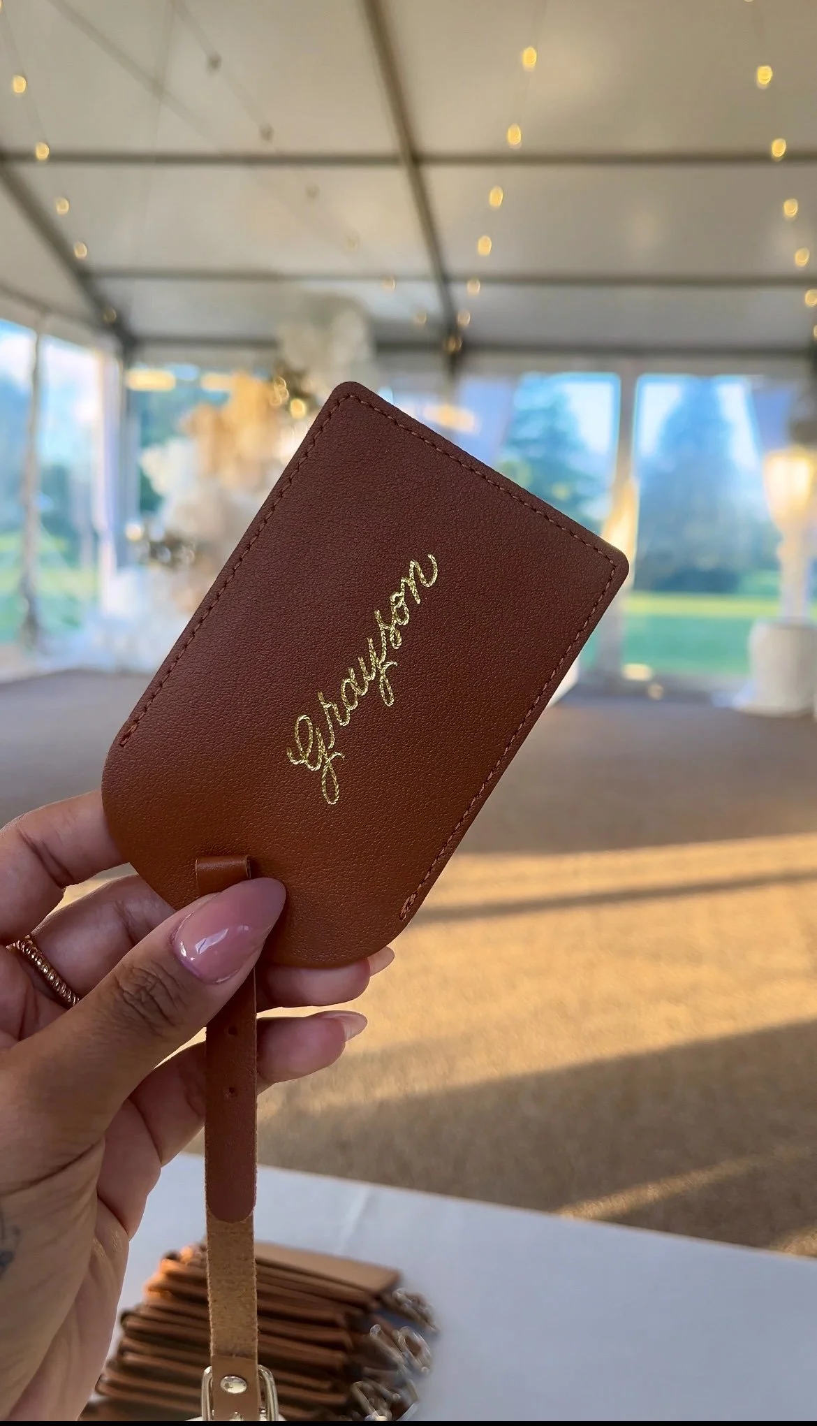 A person's hand holding a custom engraved tan leather luggage tag with gold lettering