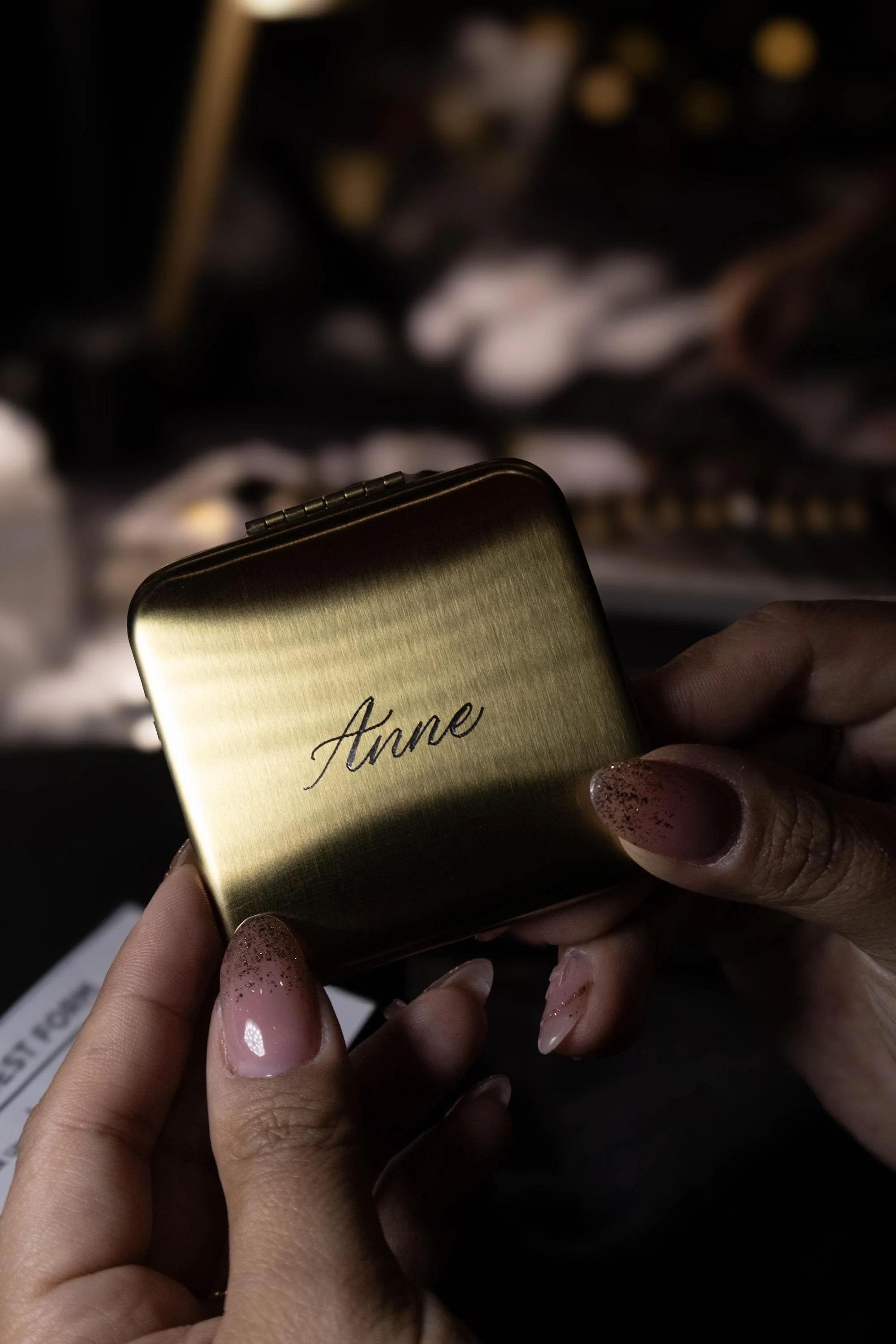Person holding a small, gold compact mirror with the name 'Anne' enrgaved on it in cursive.
