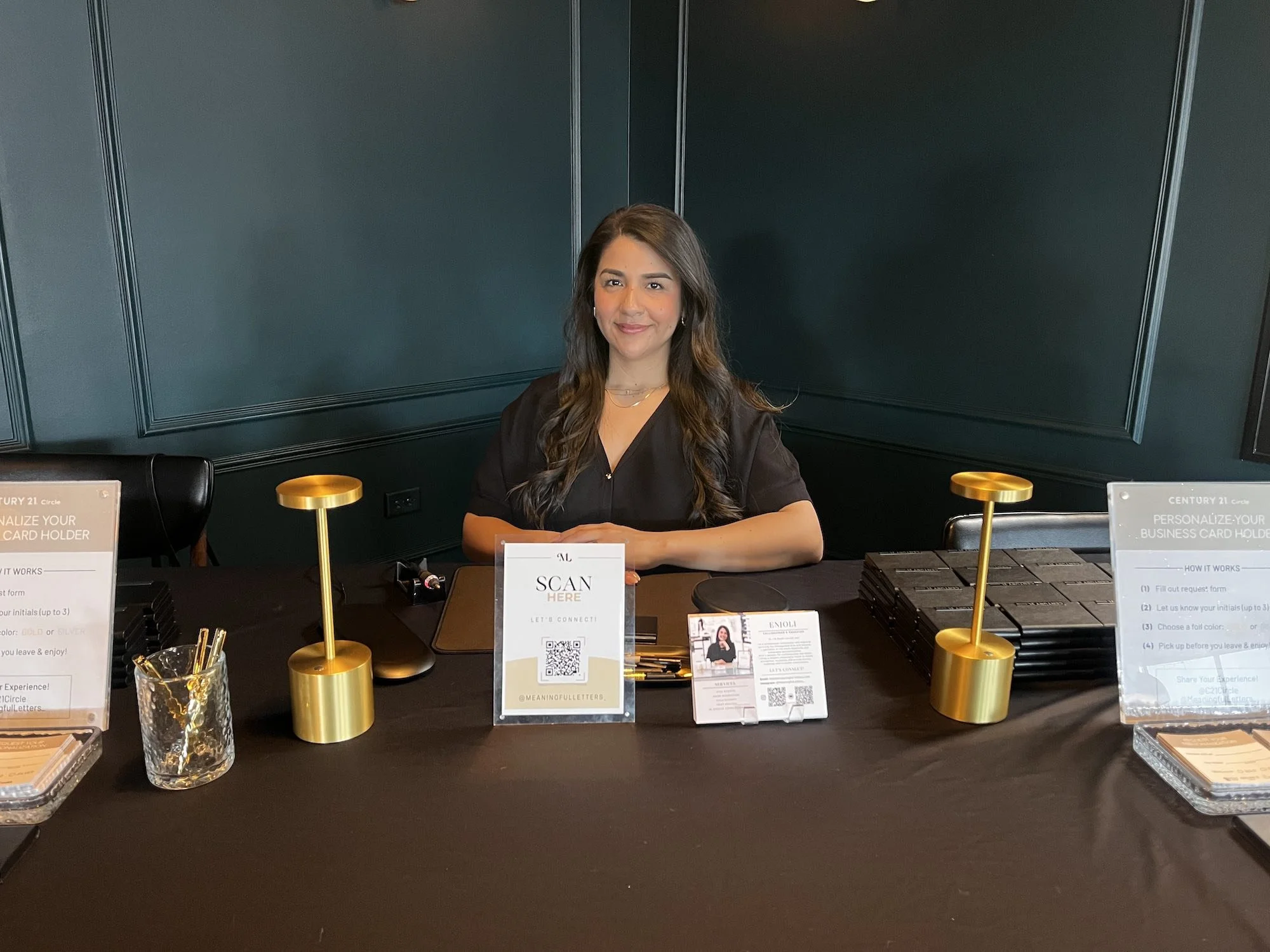 A woman sitting at a desk with a dark background, smiling.