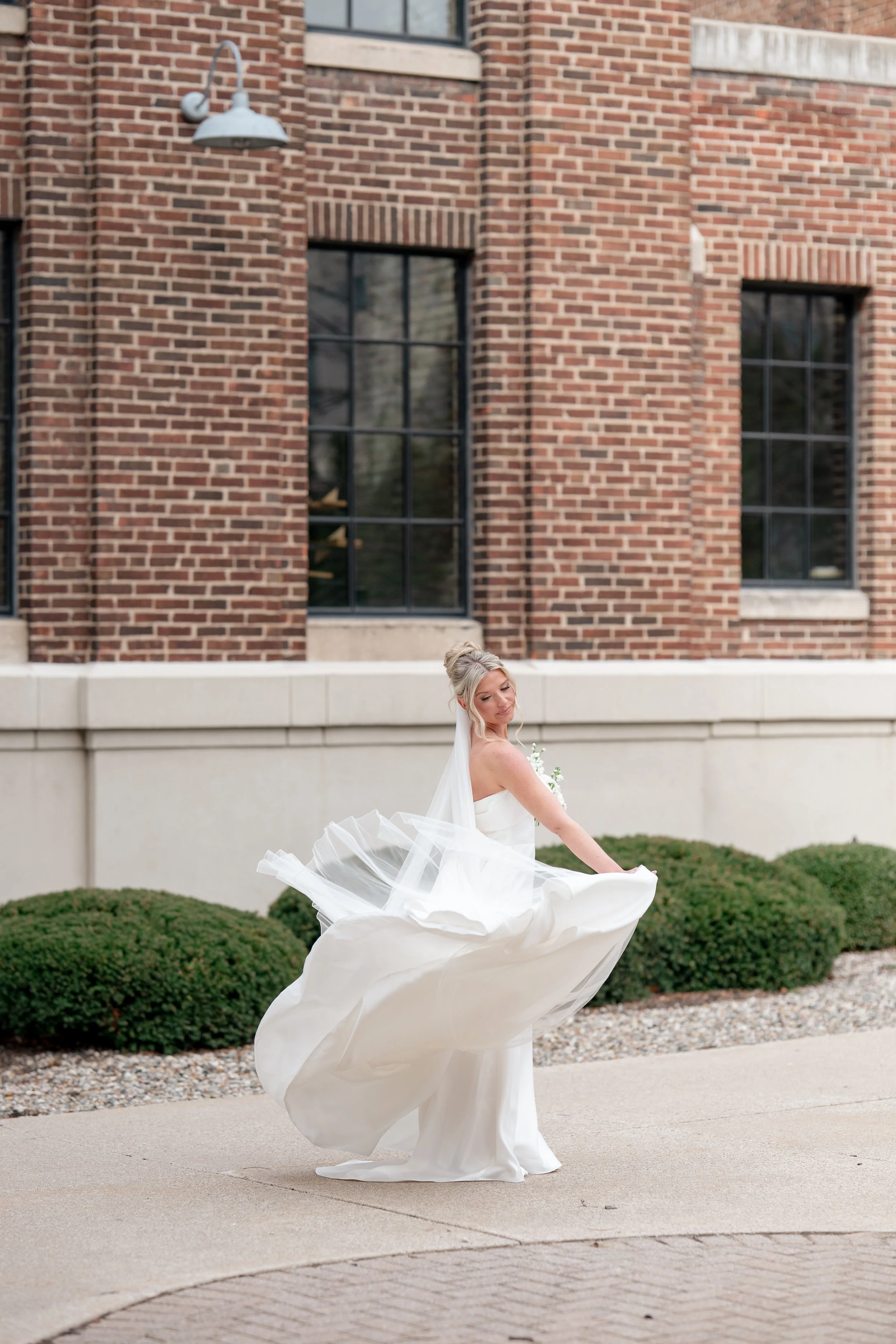 Bride twirling in her dress with a long train in front of a brick building at New Vintage Place in Grand Rapids Michigan.