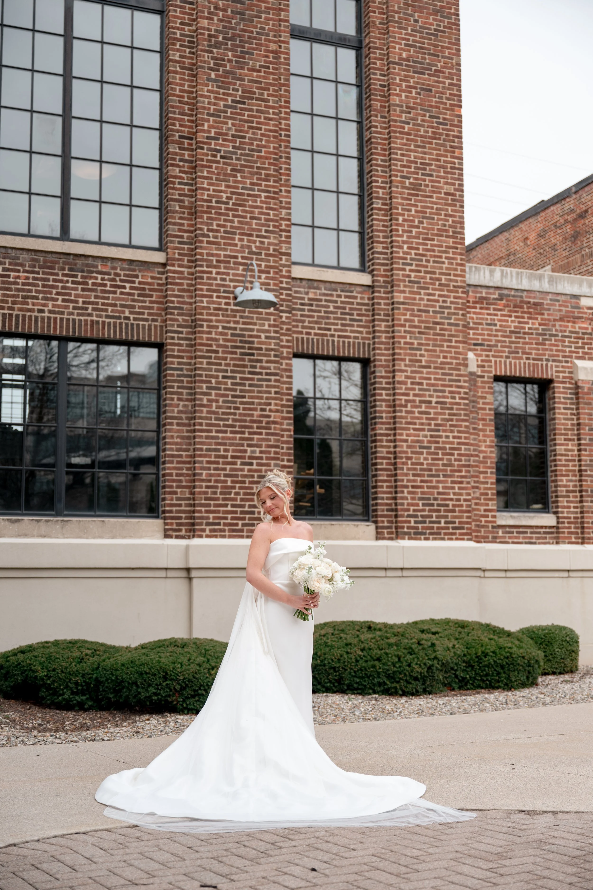 Bride standing holding her flowers and over her shoulder in front of a brick building in Grand Rapids Michigan.