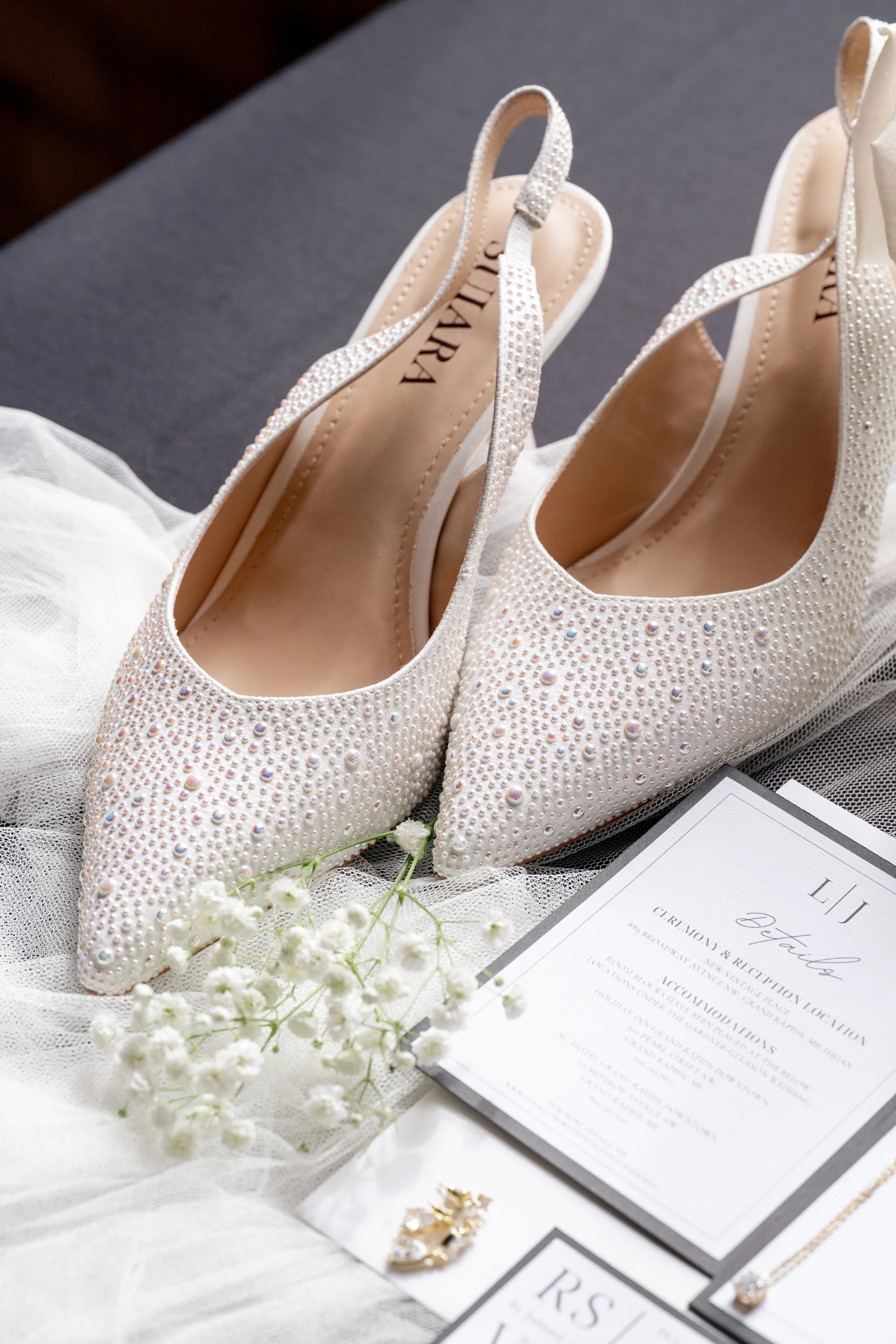 Shoes, flowers, and invitations in a flat lay setup.