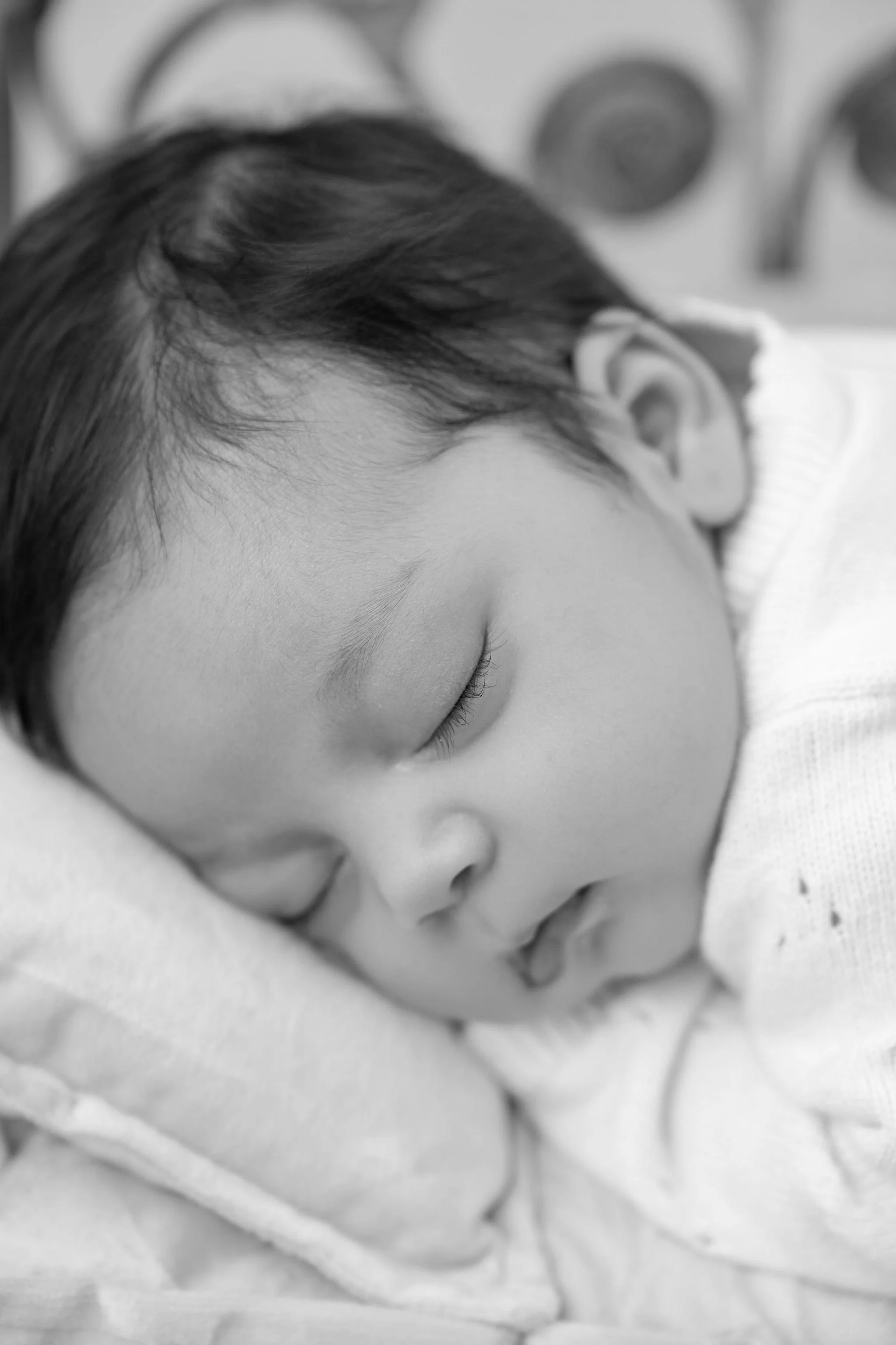 Close-up of a sleeping young child with dark hair, resting peacefully, on a soft surface.