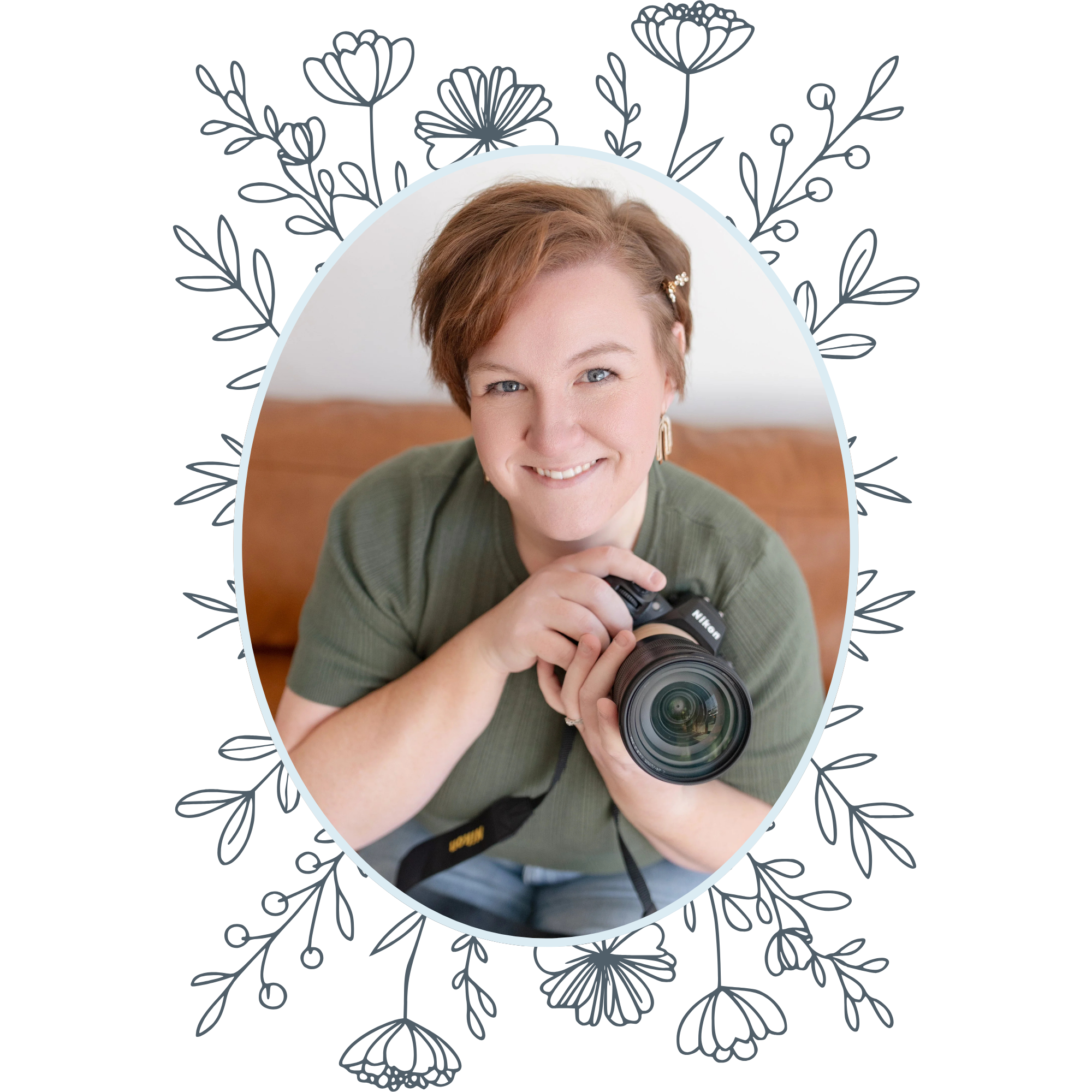 A woman with short red hair, smiling, holding a professional camera, sitting on a sofa in a cozy room.
