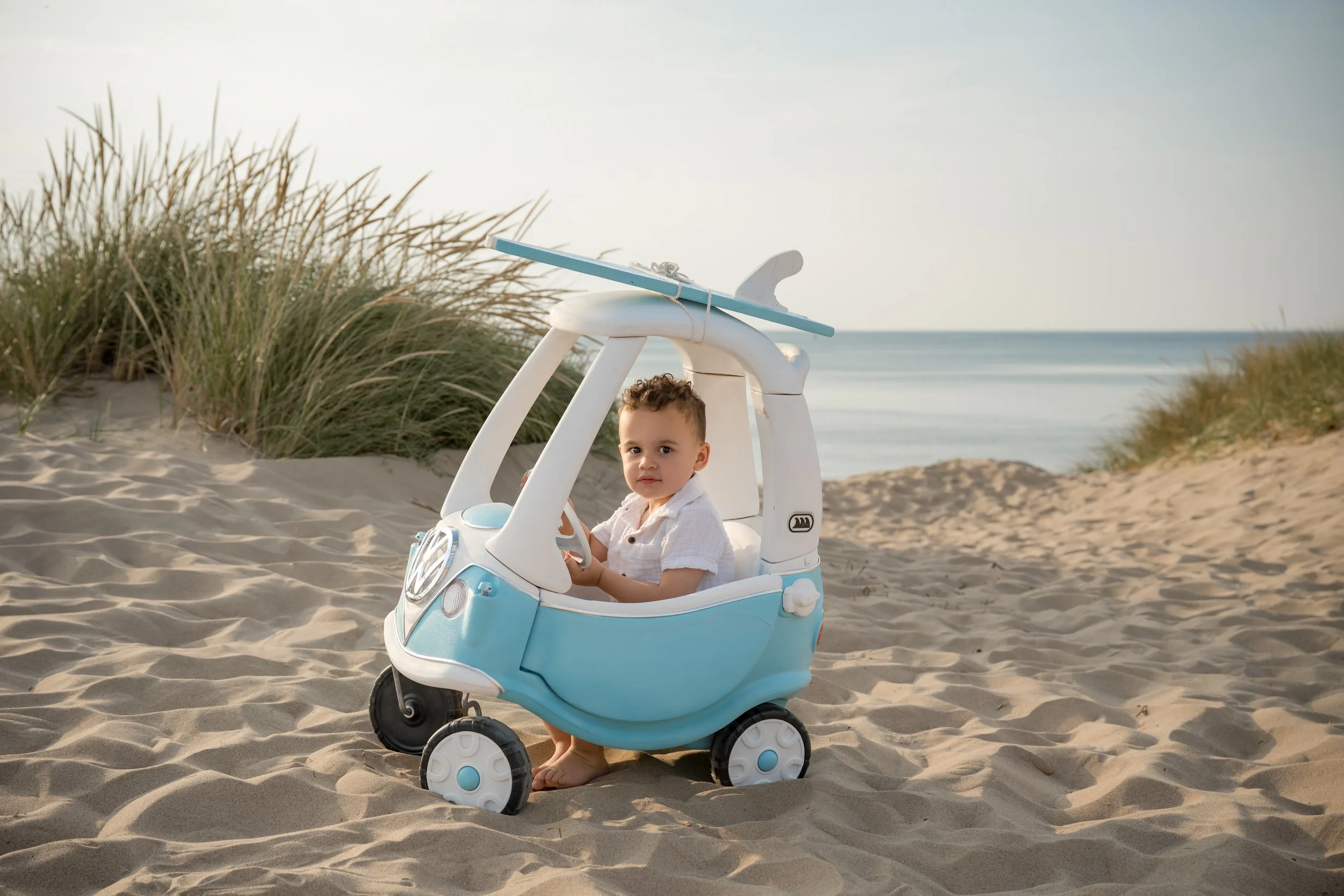 Toddler on the beach posing with a blue cozy coupe that looks like a VW bus, Holland Child Photographer