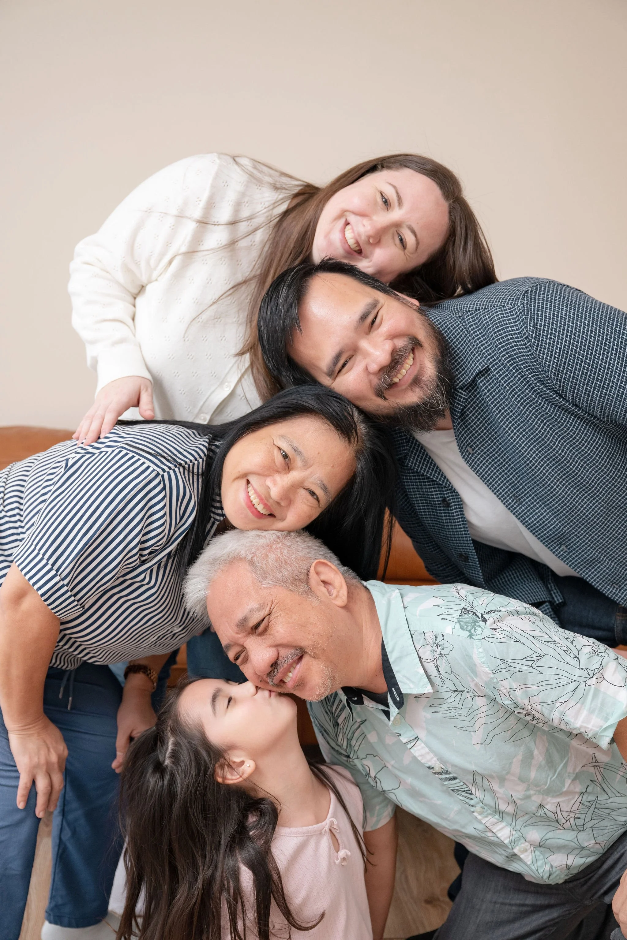 Family with their heads stacked on each other and smiling with the little girl kissing her uncle from the bottom