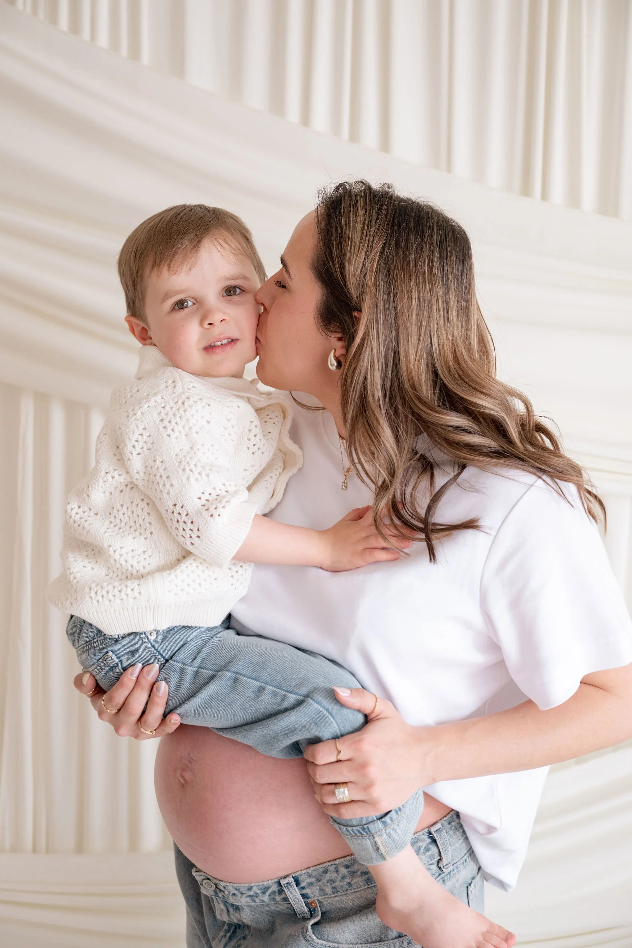 Pregnant mom kissing her toddlers cheek while holding him on her pregnant belly