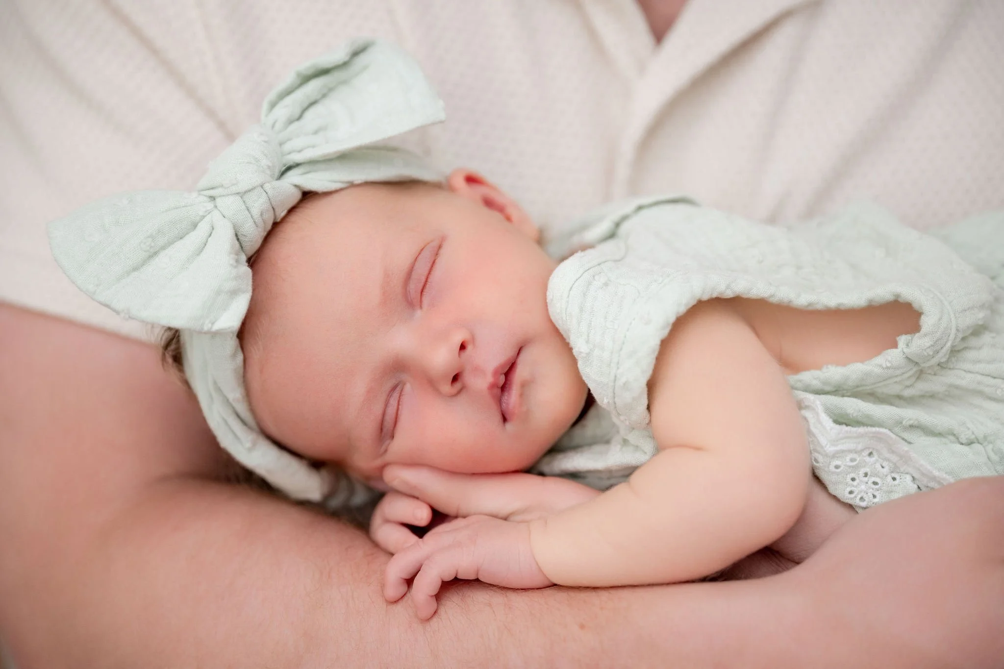 Baby wearing a light green outfit laying on dads arm