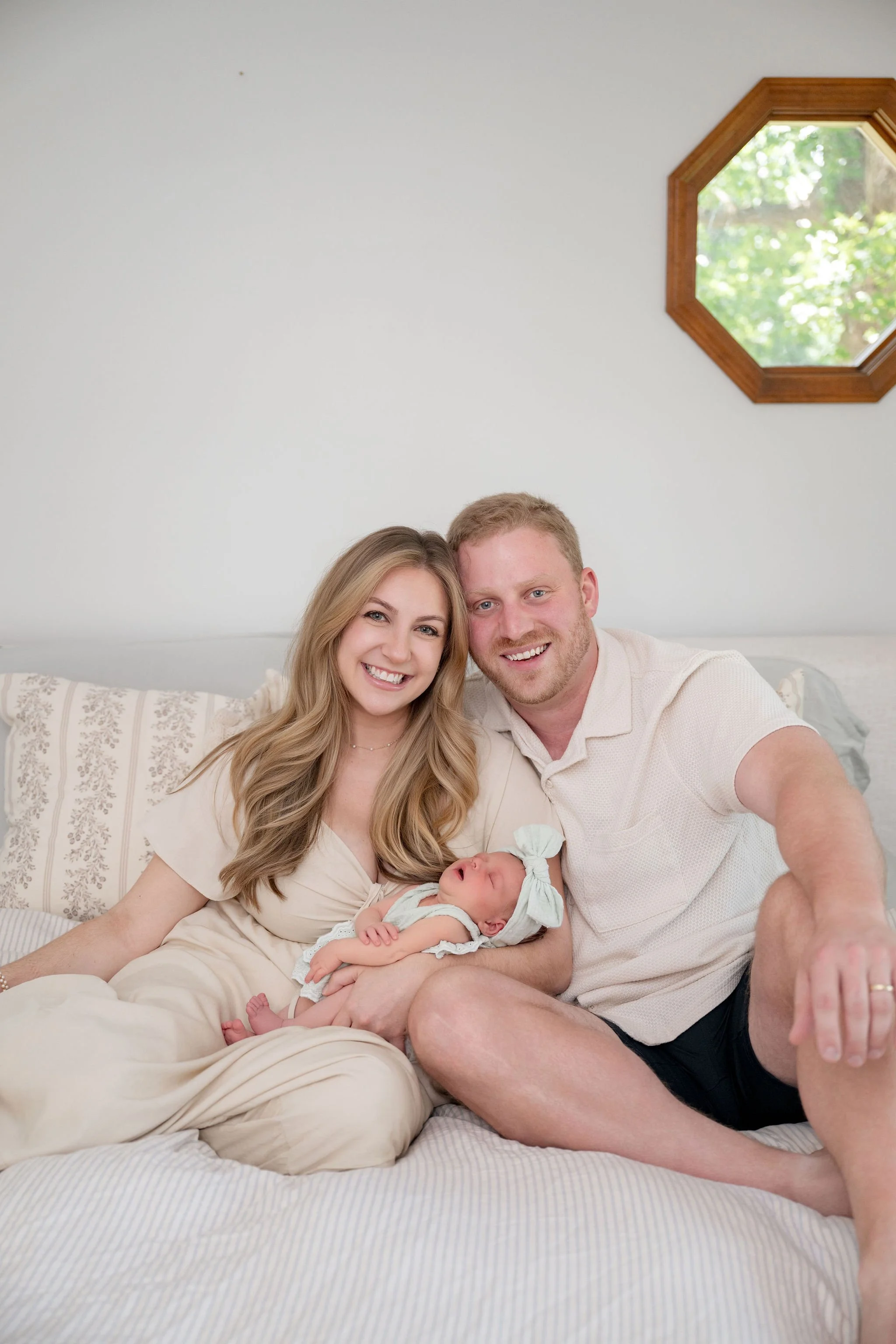 Mom, dad, and baby sitting on bed smiling