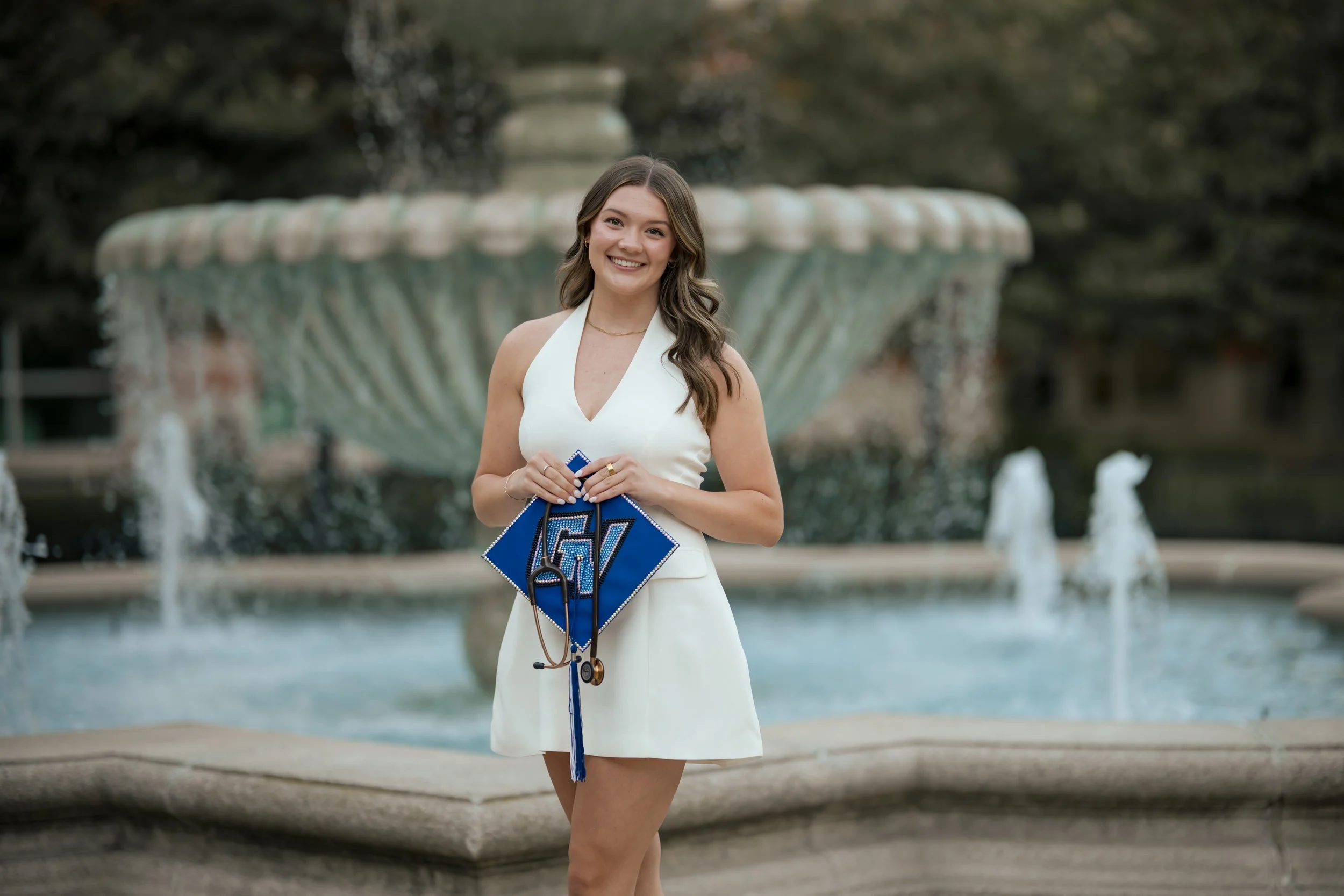 Grand Valley Cap & Gown Session with a senior wearing a white dress posing in front of a fountain on campus, Allendale Senior PHotography