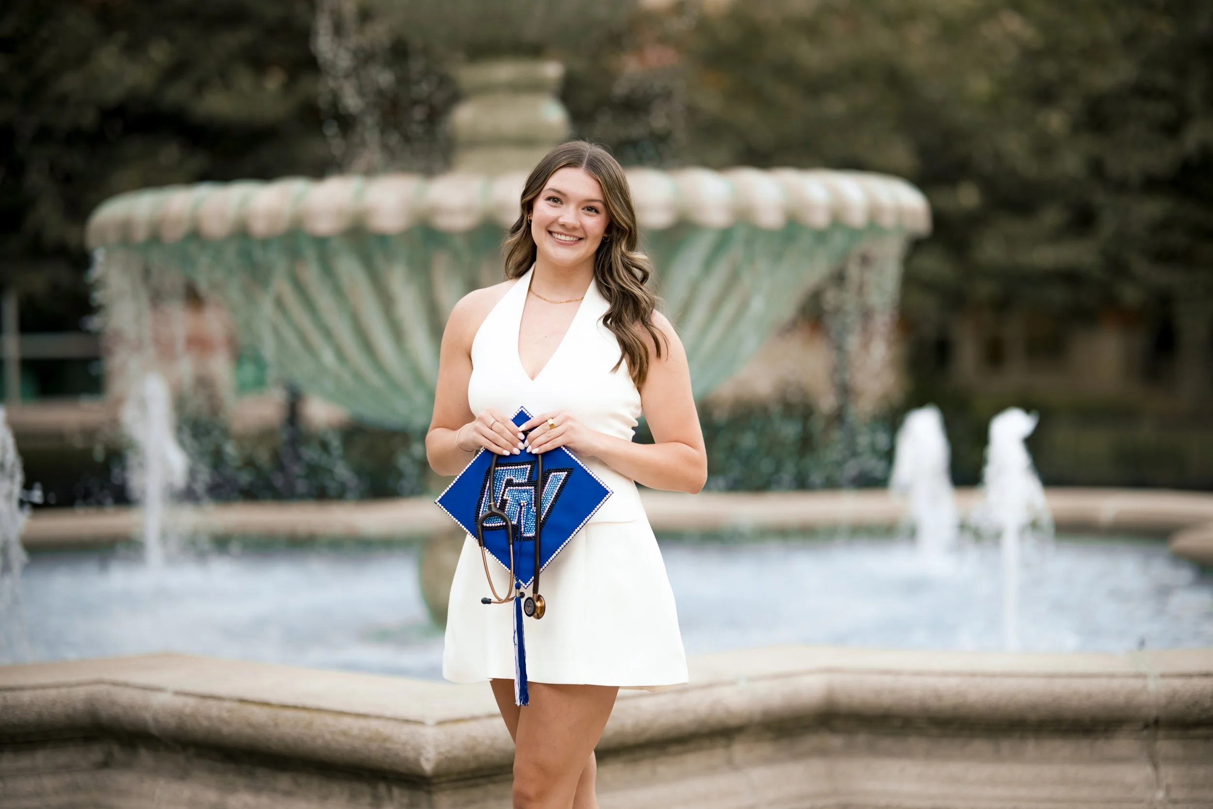 Grand Valley Senior posing in front of a fountain with their cap, cap & gown session in grand rapids Michigan