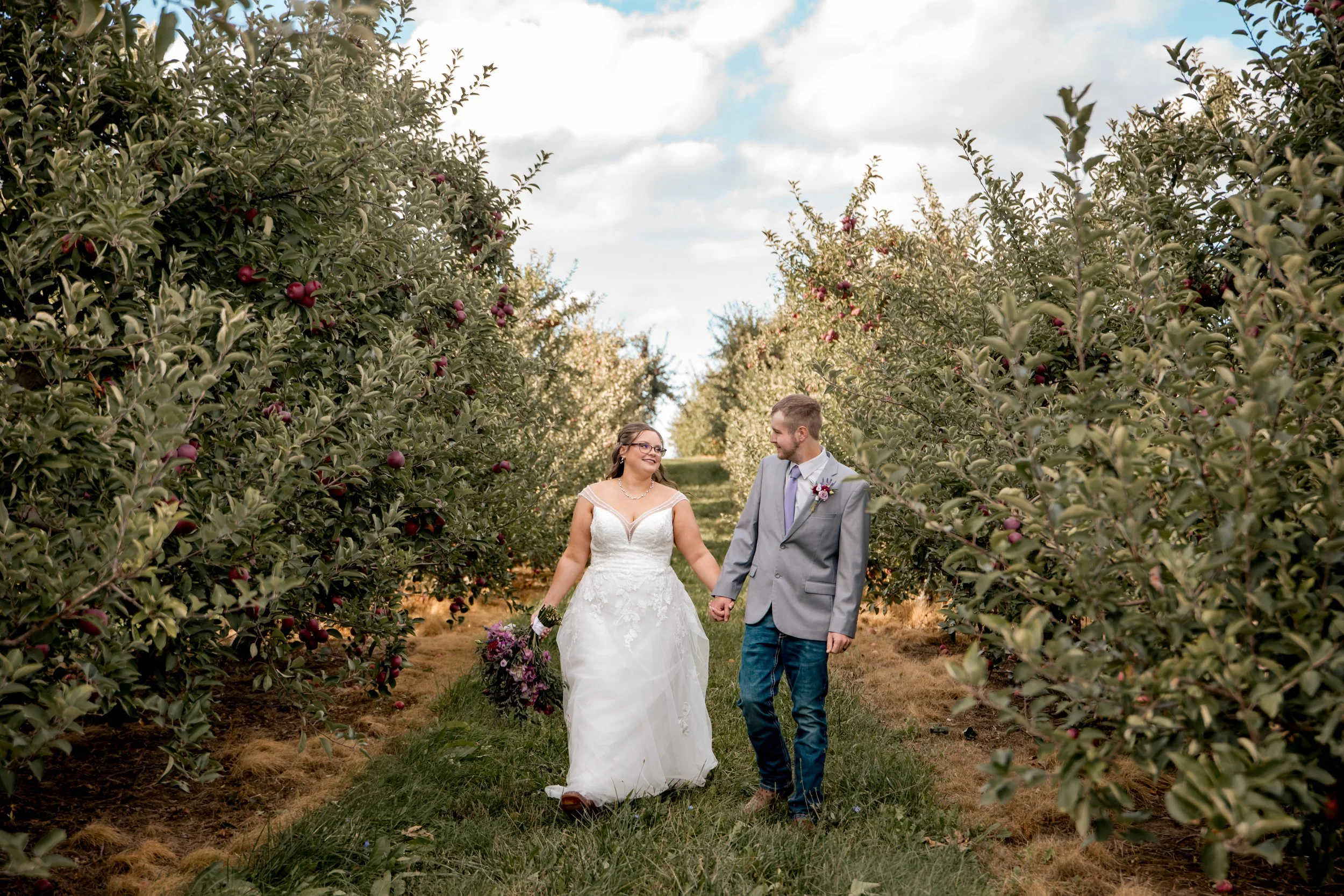 Bride and groom walking through an apple orchard on their West Michigan wedding day