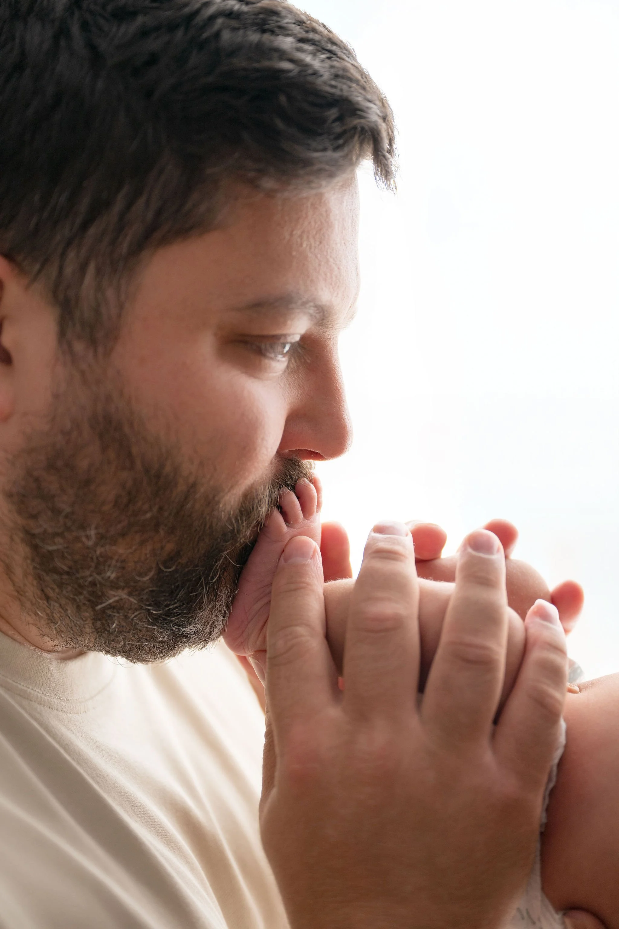 A close-up of a man with dark hair and a beard, holding and kissing a small baby or infant.