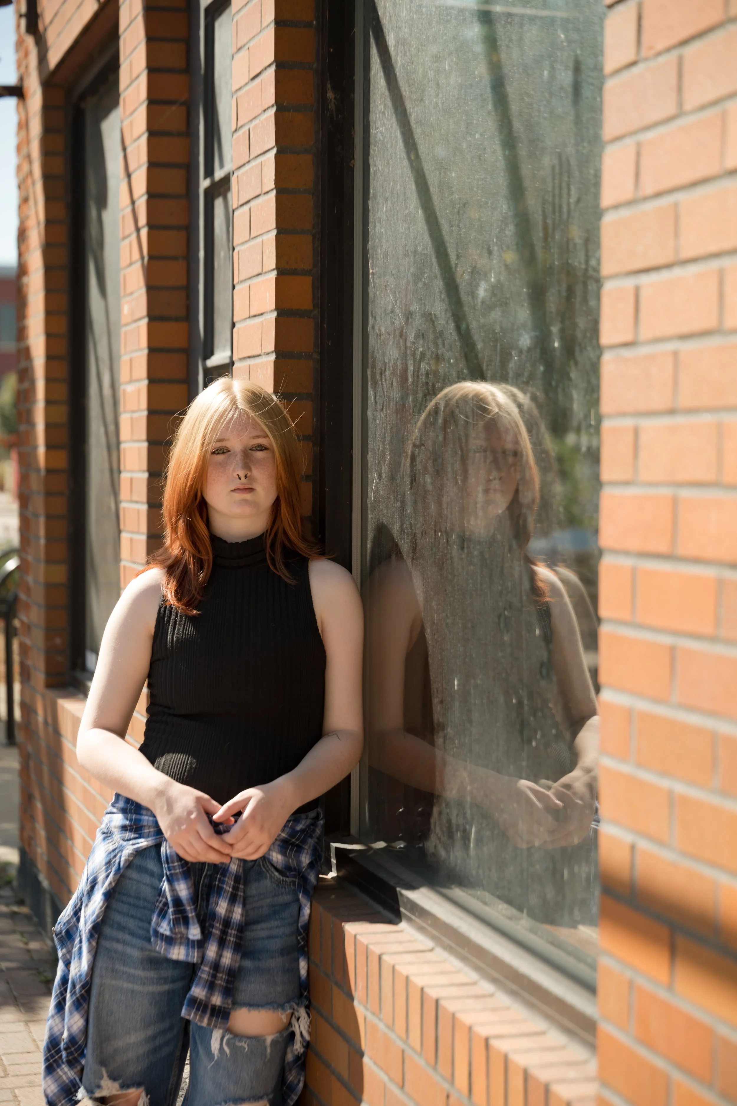 High school senior posing along a brick building with a window casting a reflection on a sunny day. Grand Rapids Senior PHotographer