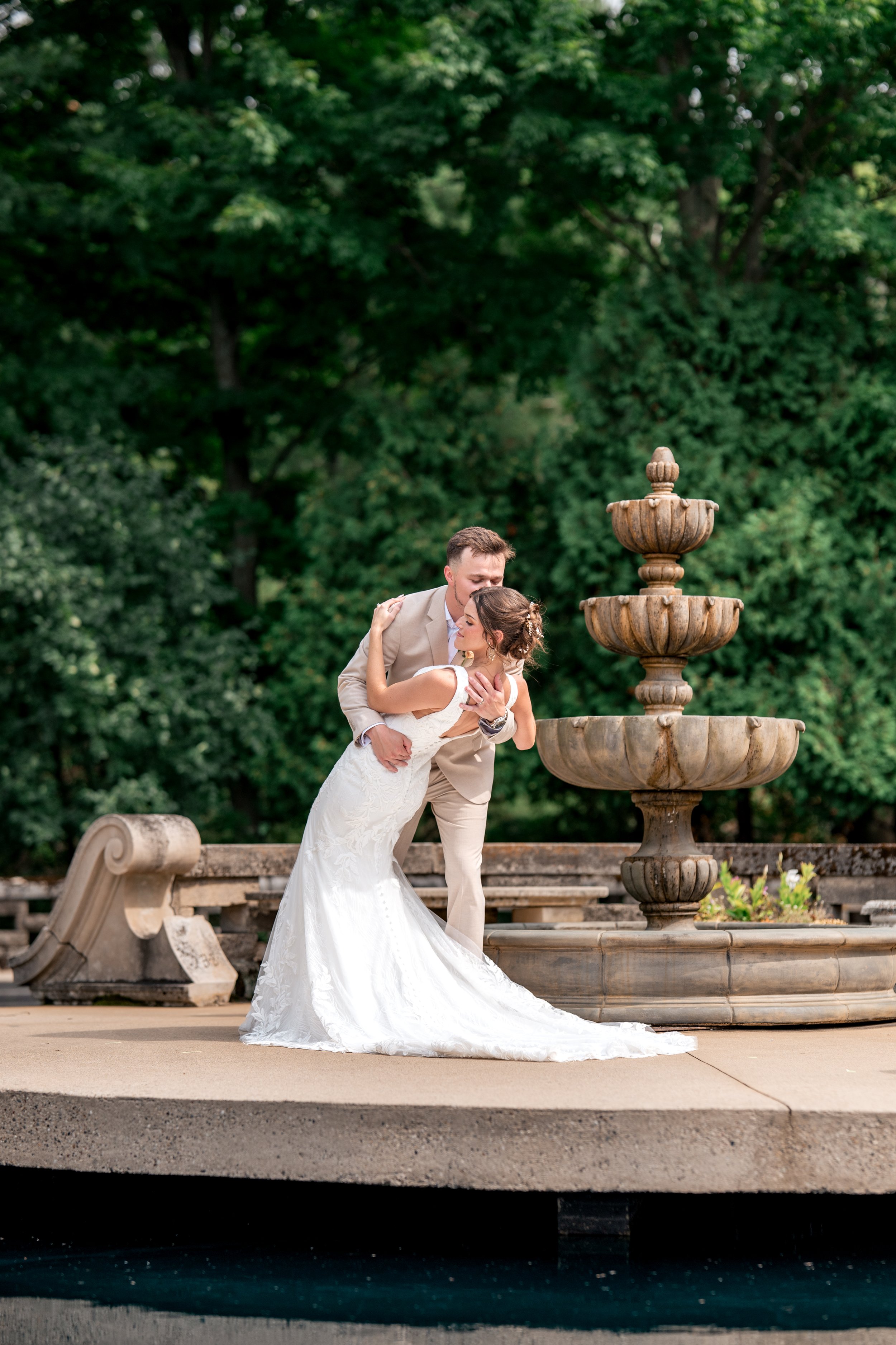A couple kissing by a fountain with greenery in the background on their wedding day. Grand rapids wedding photographer