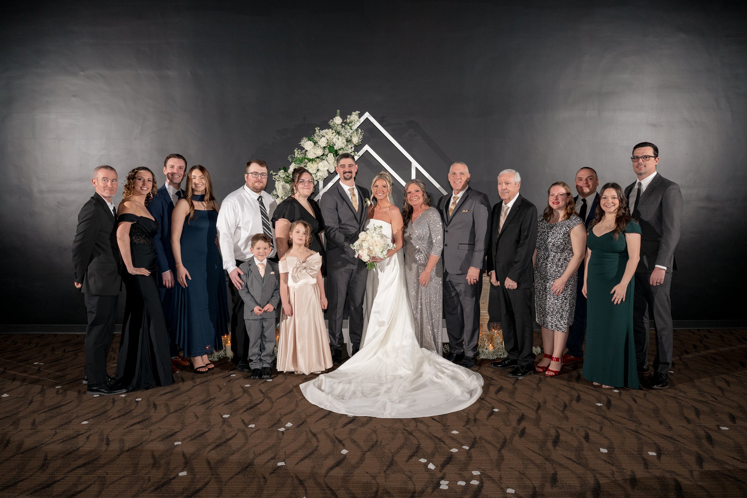Bride and groom posed with family against a black backdrop.