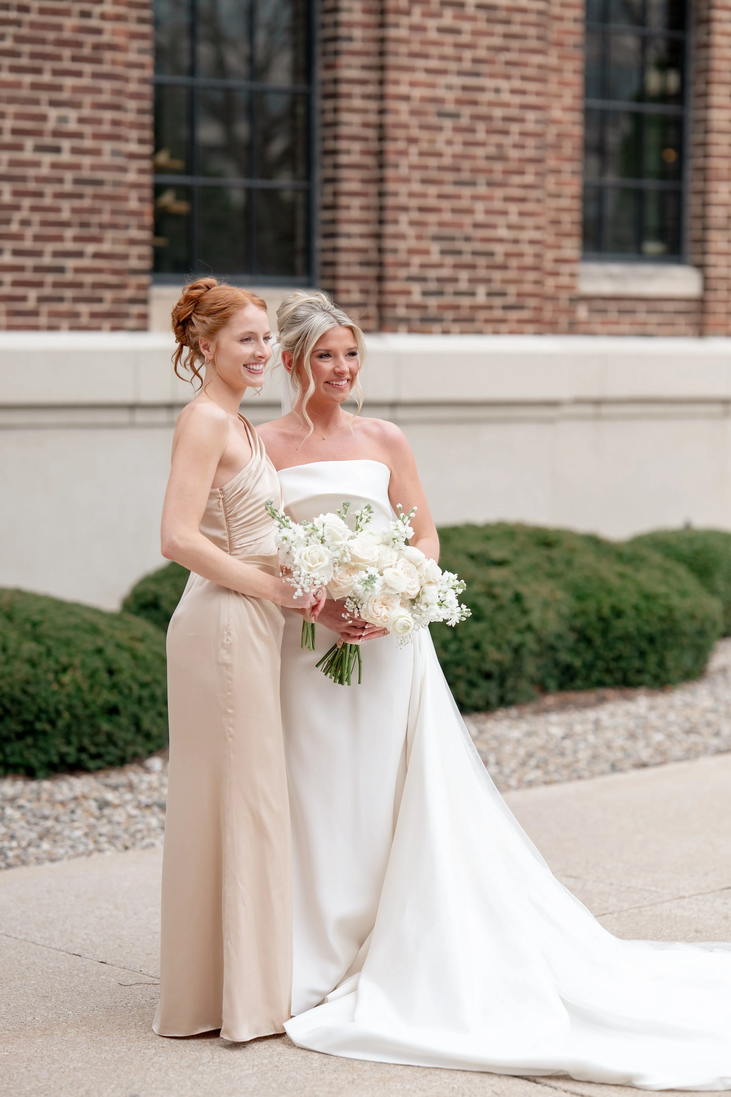 Bride and bridesmaid standing next to each other for a photograph.