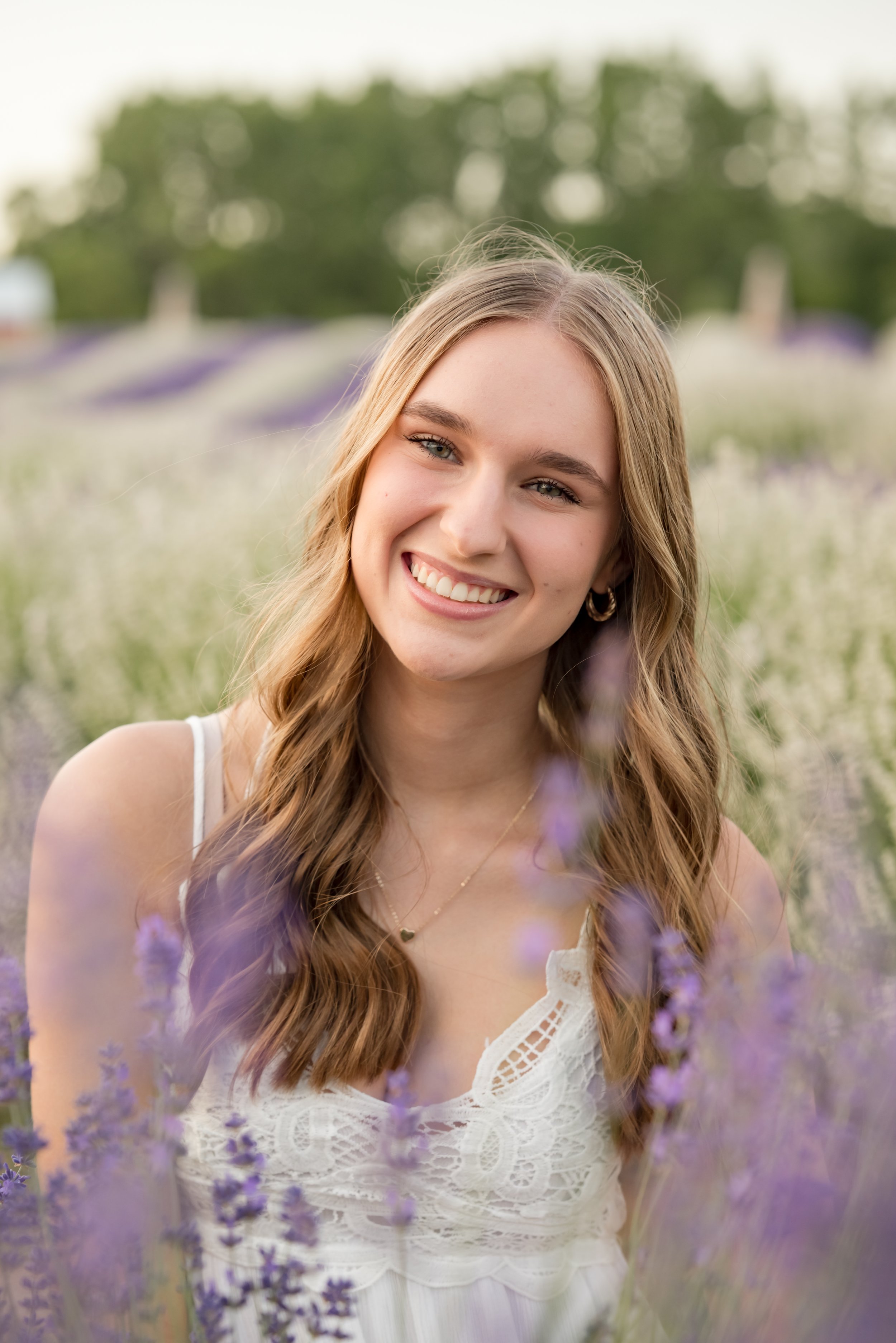 A young woman with long wavy brown hair smiling in a lavender field.