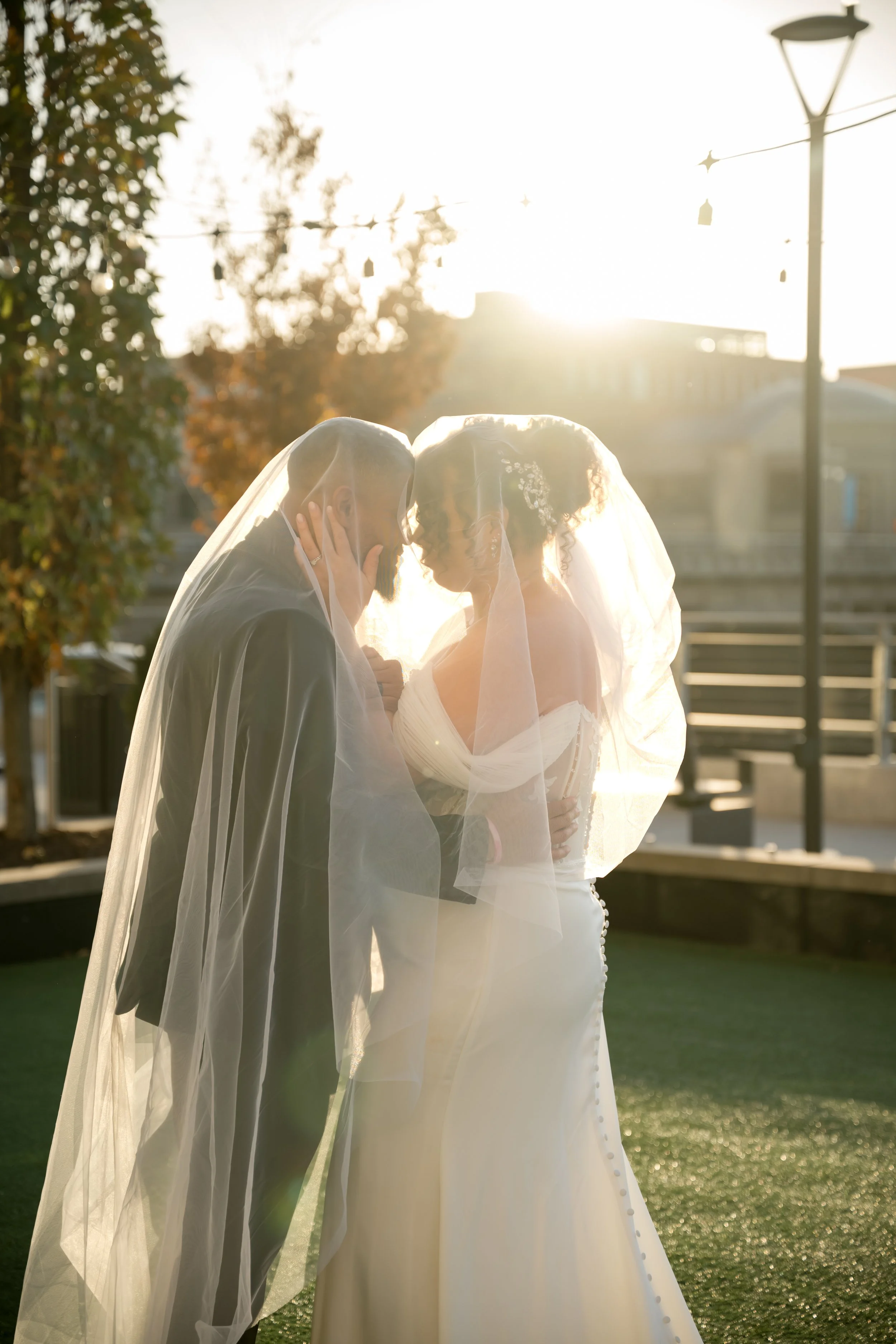 Bride and groom share a backlit kiss beneath her veil at a West Michigan wedding