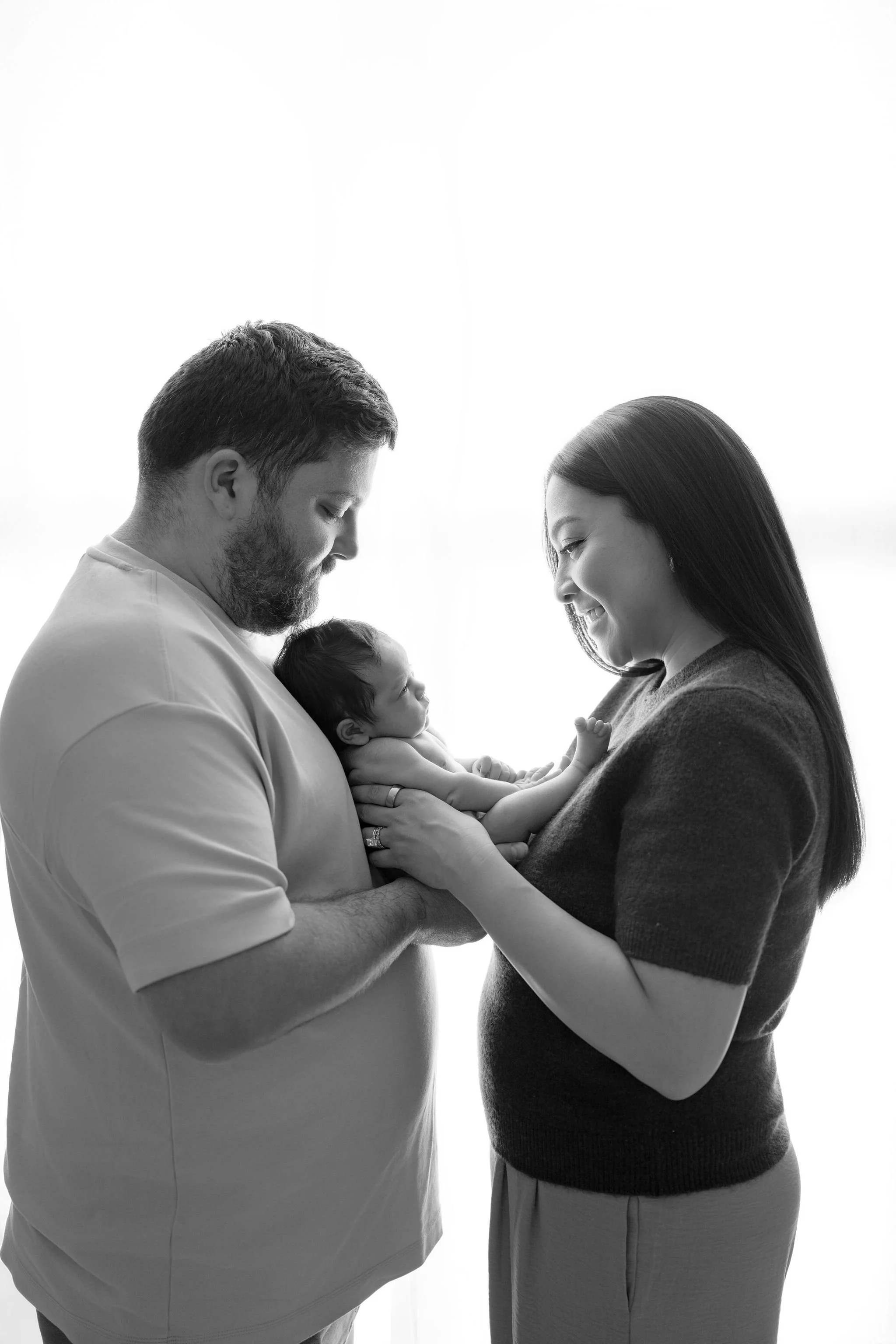 A black and white photo of a man and a woman holding a newborn baby, looking at the baby affectionately.