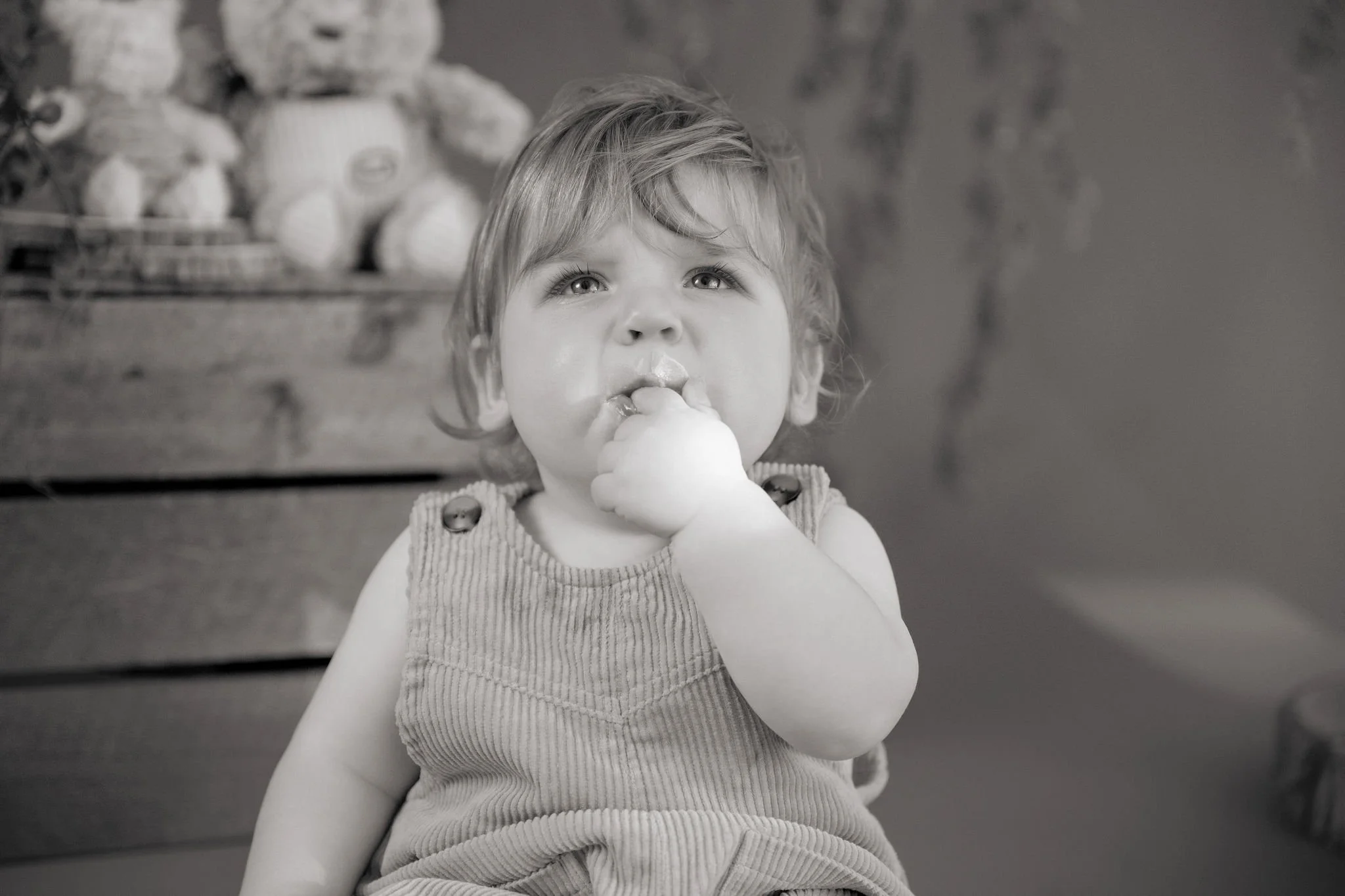 A young child with curly hair sits at a table, eating what appears to be ice cream or a similar treat, with a thoughtful expression.