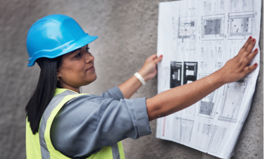 Construction worker in a blue safety helmet and reflective vest reviewing blueprints on a wall