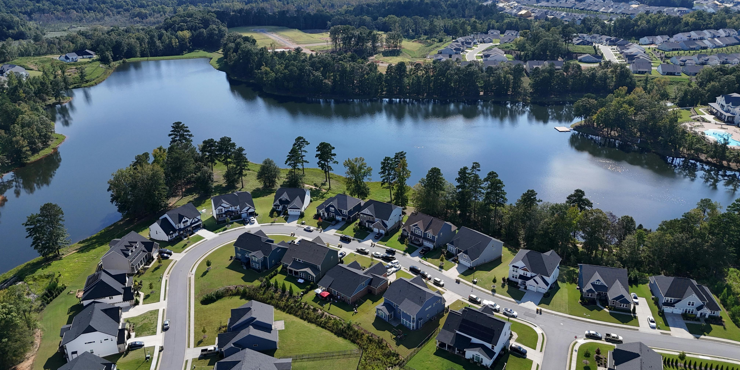 Aerial view of a suburban neighborhood with houses, streets, a lake, and surrounding greenery.