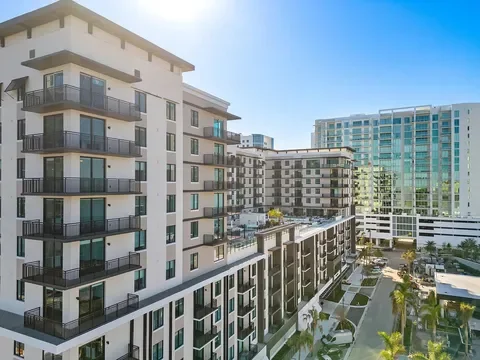 Modern apartment buildings in an urban area with balconies, glass windows, and landscaping under a clear blue sky.