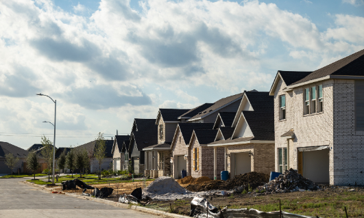 Row of new houses under construction on a suburban street with construction materials and debris in the foreground.