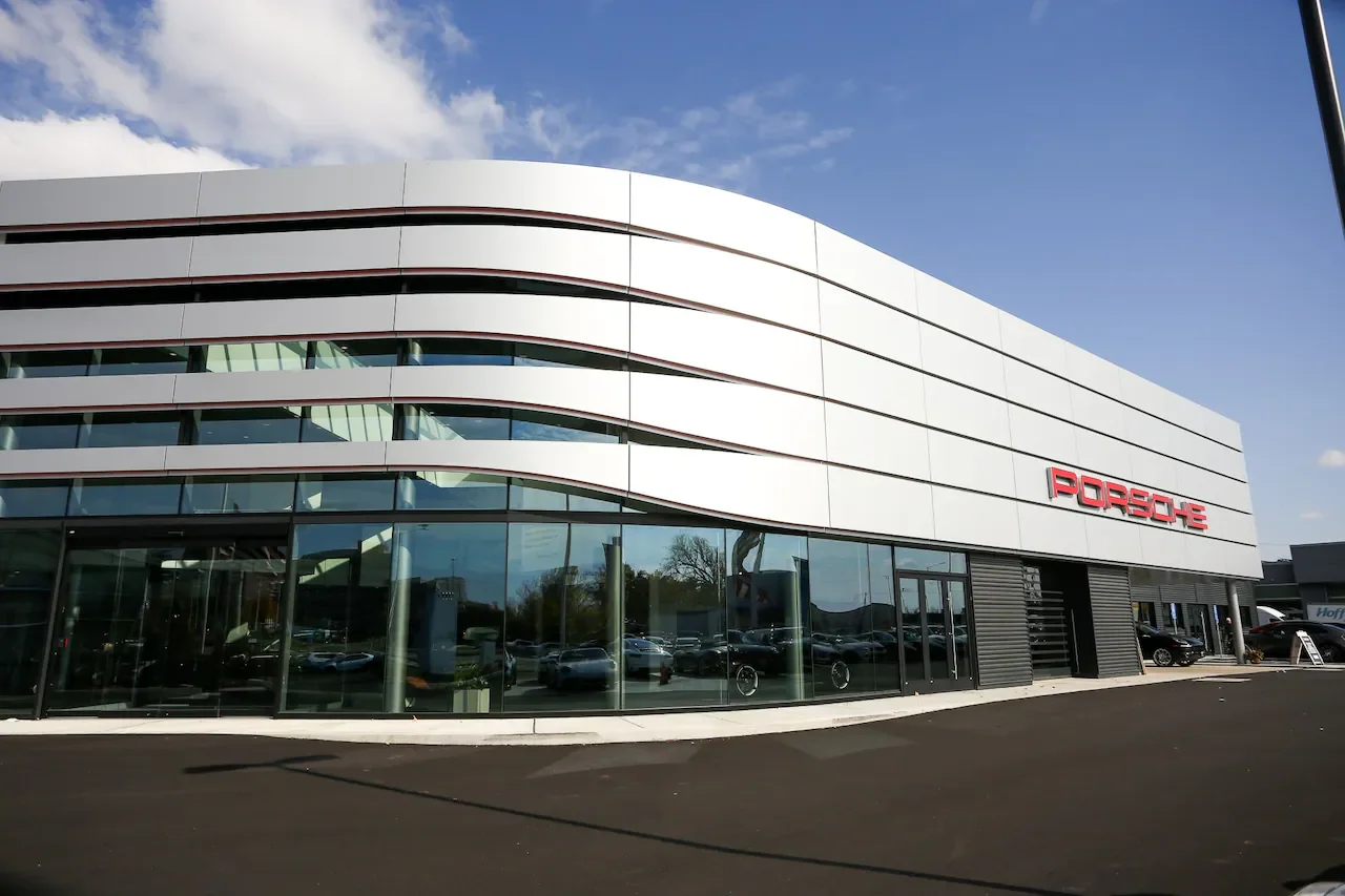Modern Porsche car dealership with a white exterior, large glass windows, and the Porsche logo in red on the front.