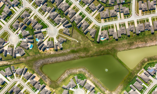 Aerial view of a residential neighborhood with a pond at the center and small houses surrounding it.