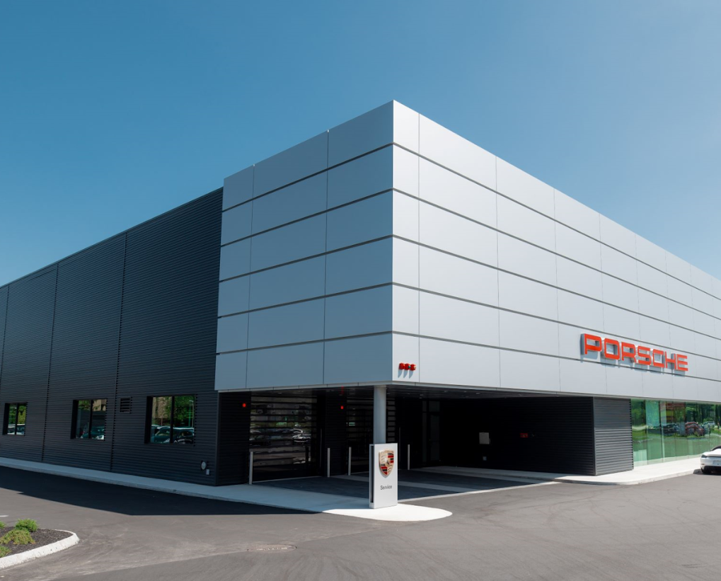 Modern Porsche dealership building with black and white exterior panels and a red Porsche logo, under a clear blue sky.