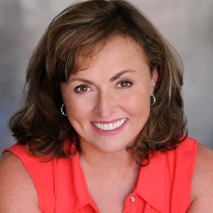 A woman with medium-length brown hair and brown eyes, smiling and wearing a sleeveless red top, with a blurred neutral background.