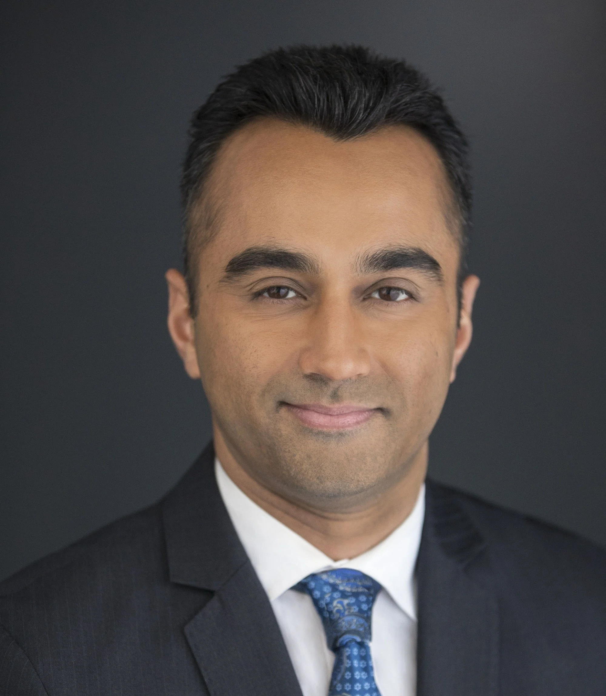 Headshot of a man in a business suit with a dark background.