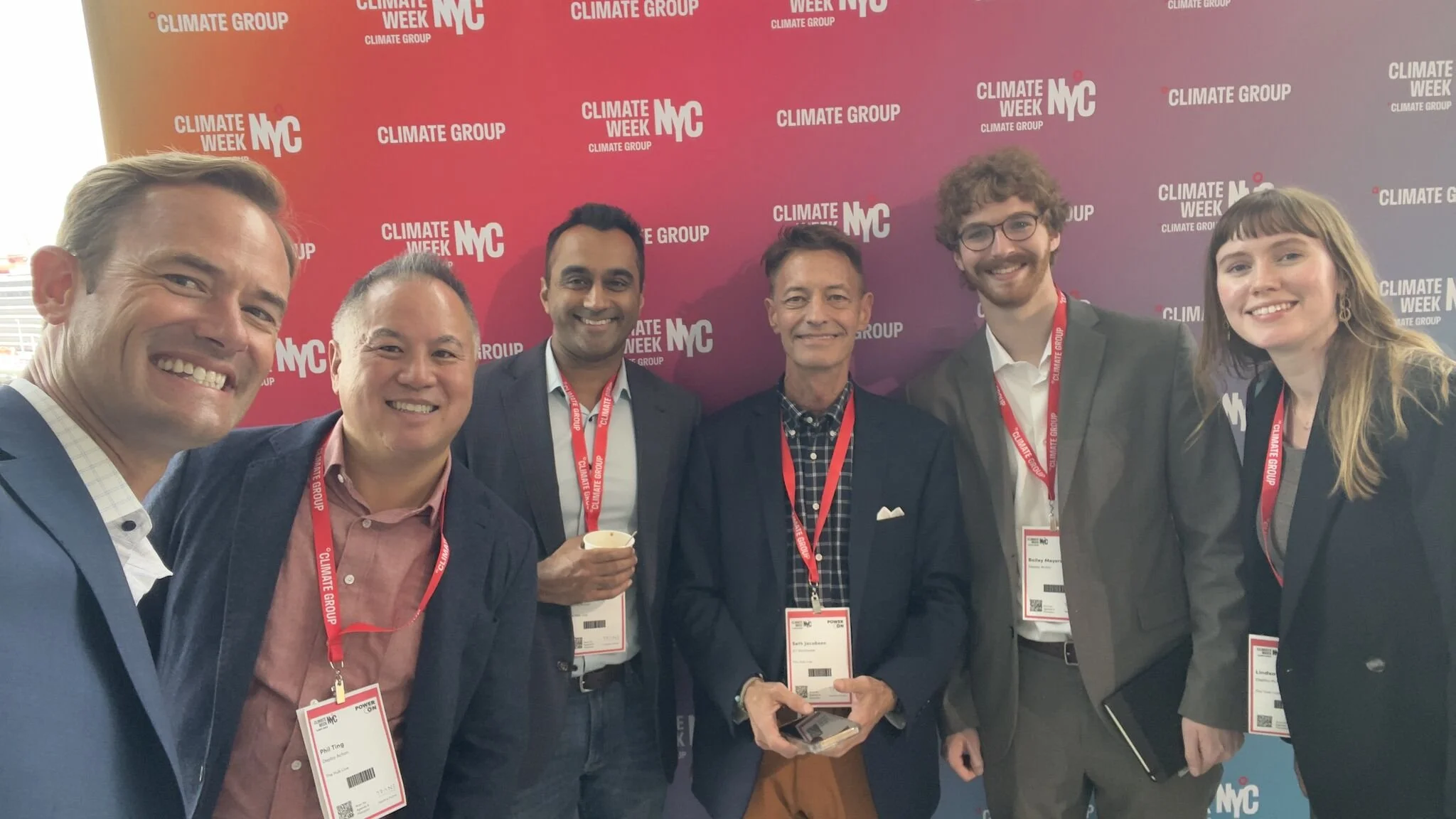 Group of seven people at Climate Week NYC, smiling and posing for a photo in front of a red and purple backdrop with 'Climate Group' and 'NYC' logos.