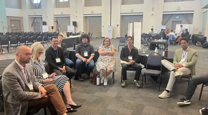 A group of seven people sitting in a semi-circle in a conference hall.