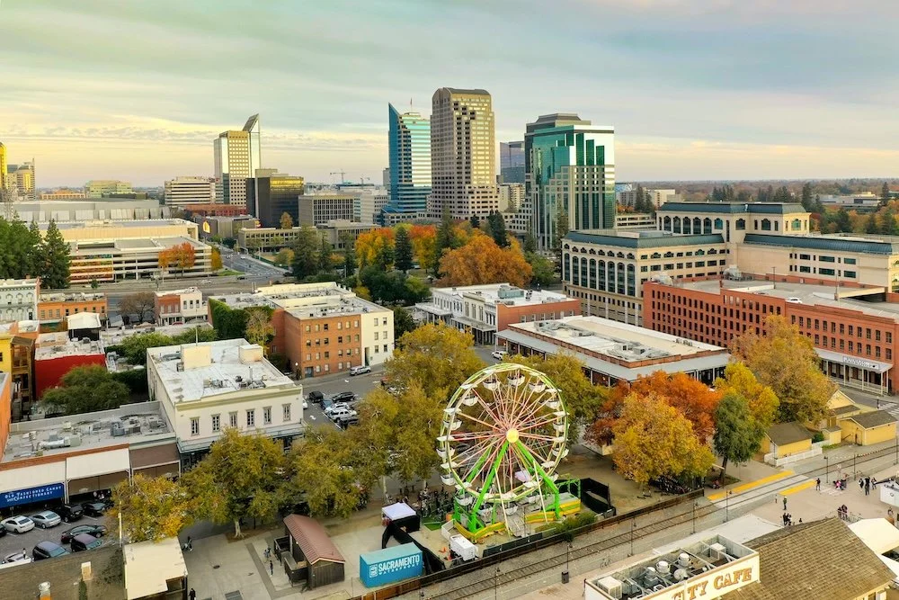 Downtown cityscape with tall modern buildings, a Ferris wheel, and trees with fall foliage.