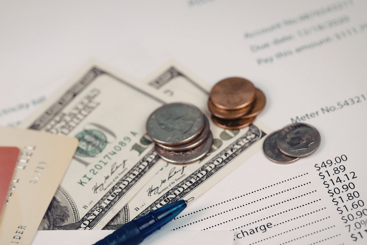 An electric bill with money covering it.