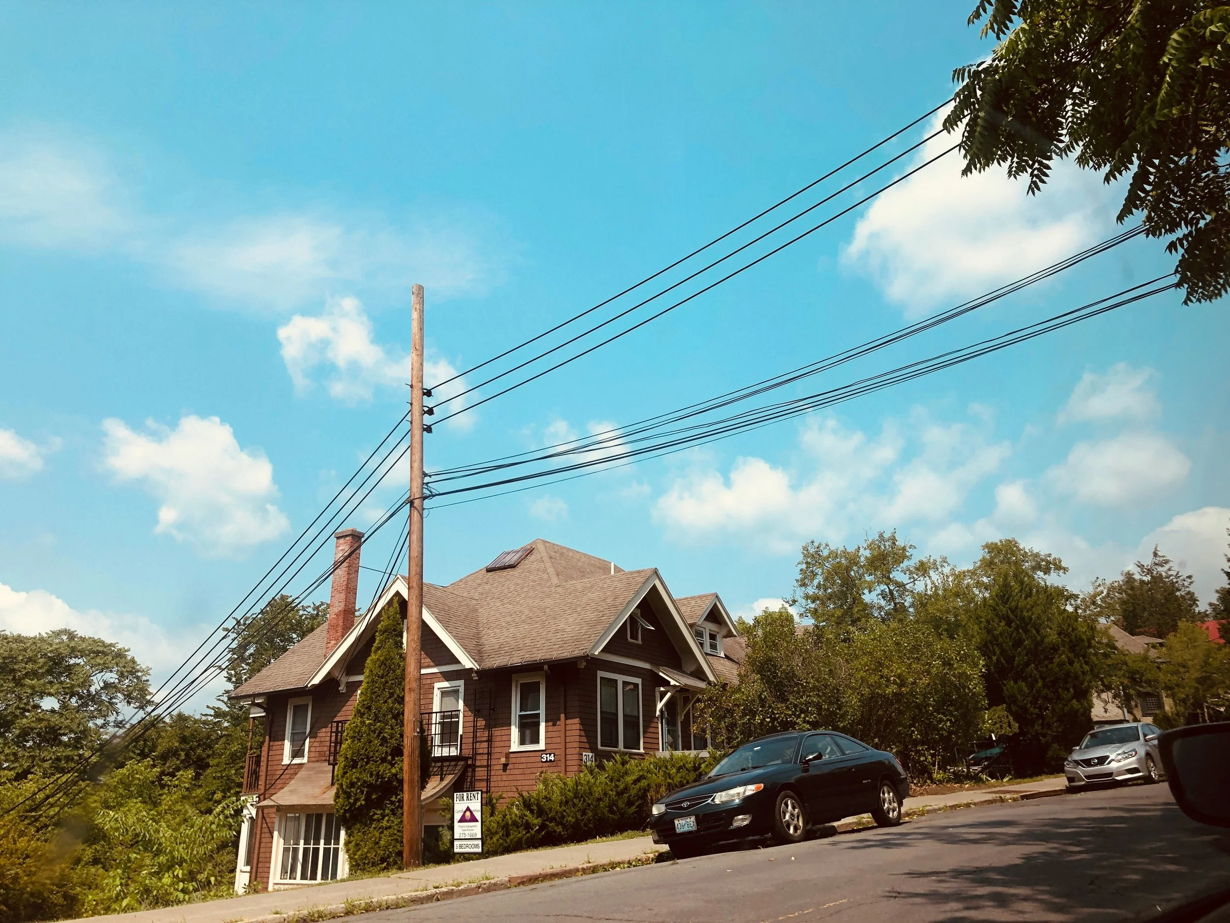 A small house with a car out front and powerlines over head.