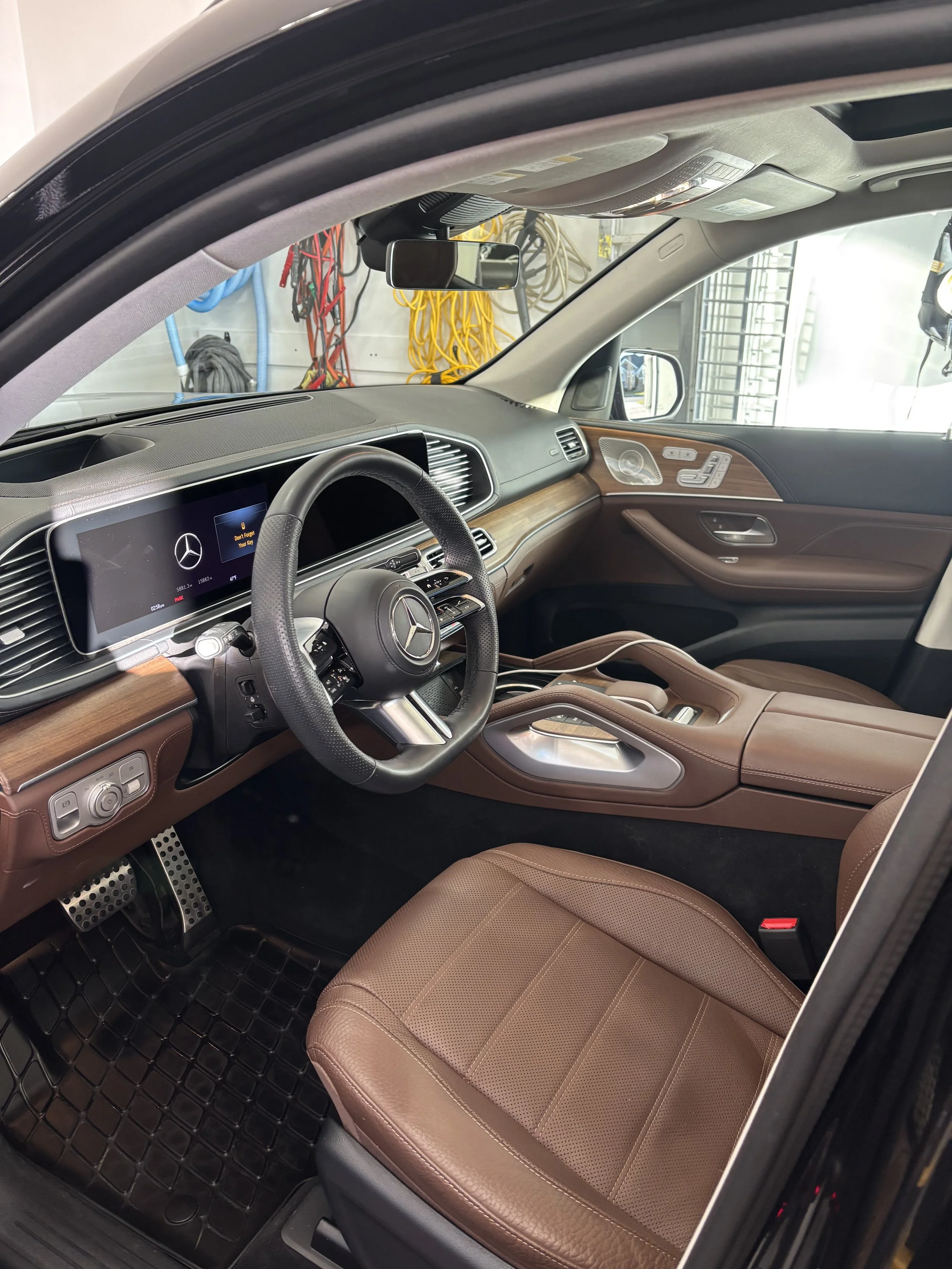 Interior of a luxury Mercedes-Benz vehicle with a brown leather seat, digital dashboard, steering wheel, and wooden accents.