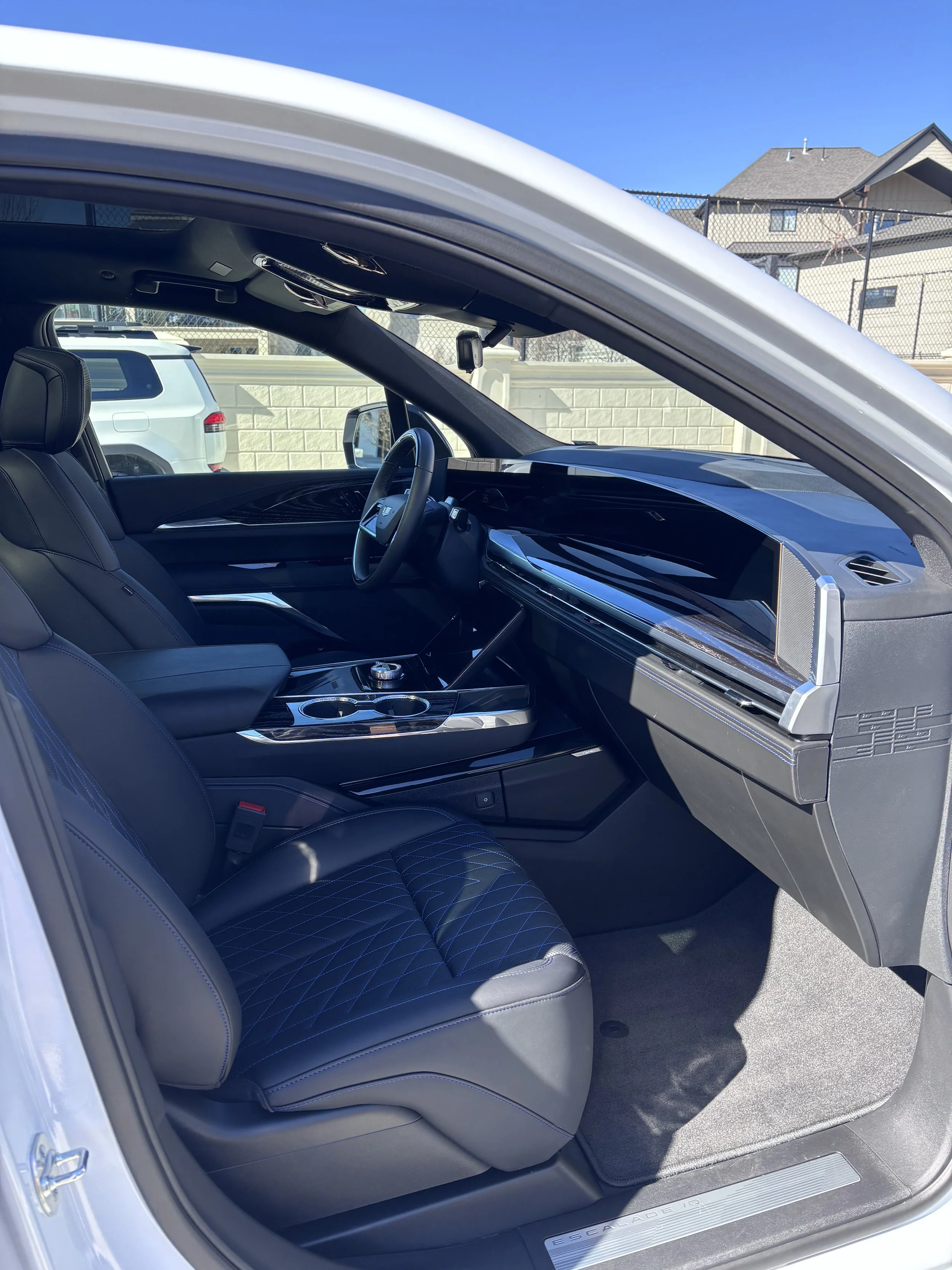 Interior of a modern car showing front seats, dashboard, steering wheel, and center console with two cup holders, parked outdoors with a blue sky in the background.