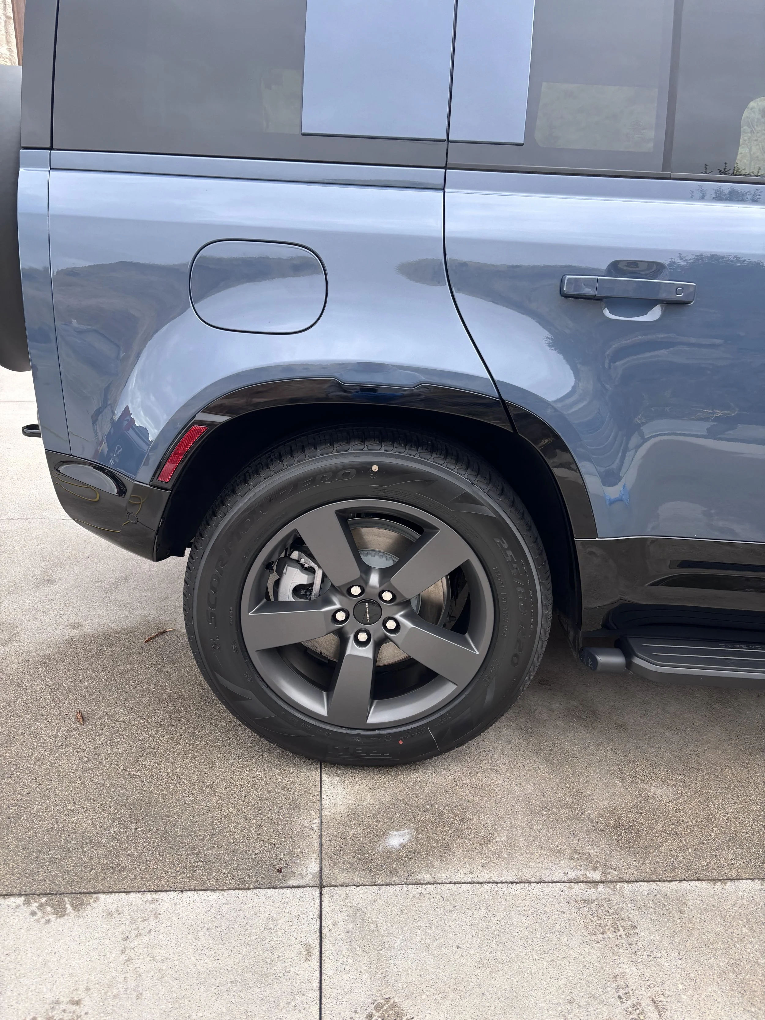 Close-up of the rear side of a modern blue SUV vehicle parked on a driveway, showing the rear wheel and part of the side panel.