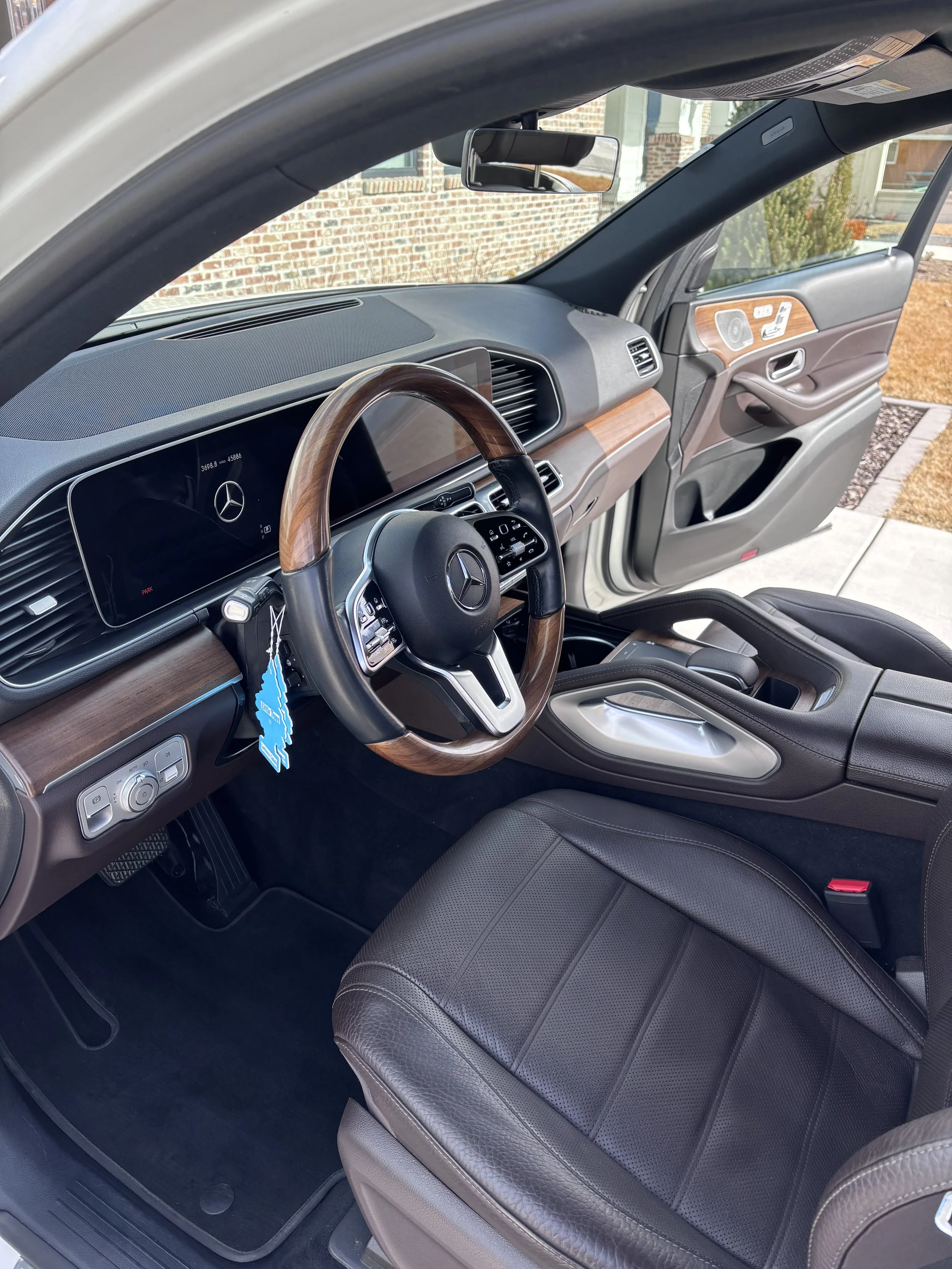 Interior of a Mercedes-Benz vehicle with black leather seats, a wooden steering wheel, a digital dashboard, and a center console with a gear shifter.