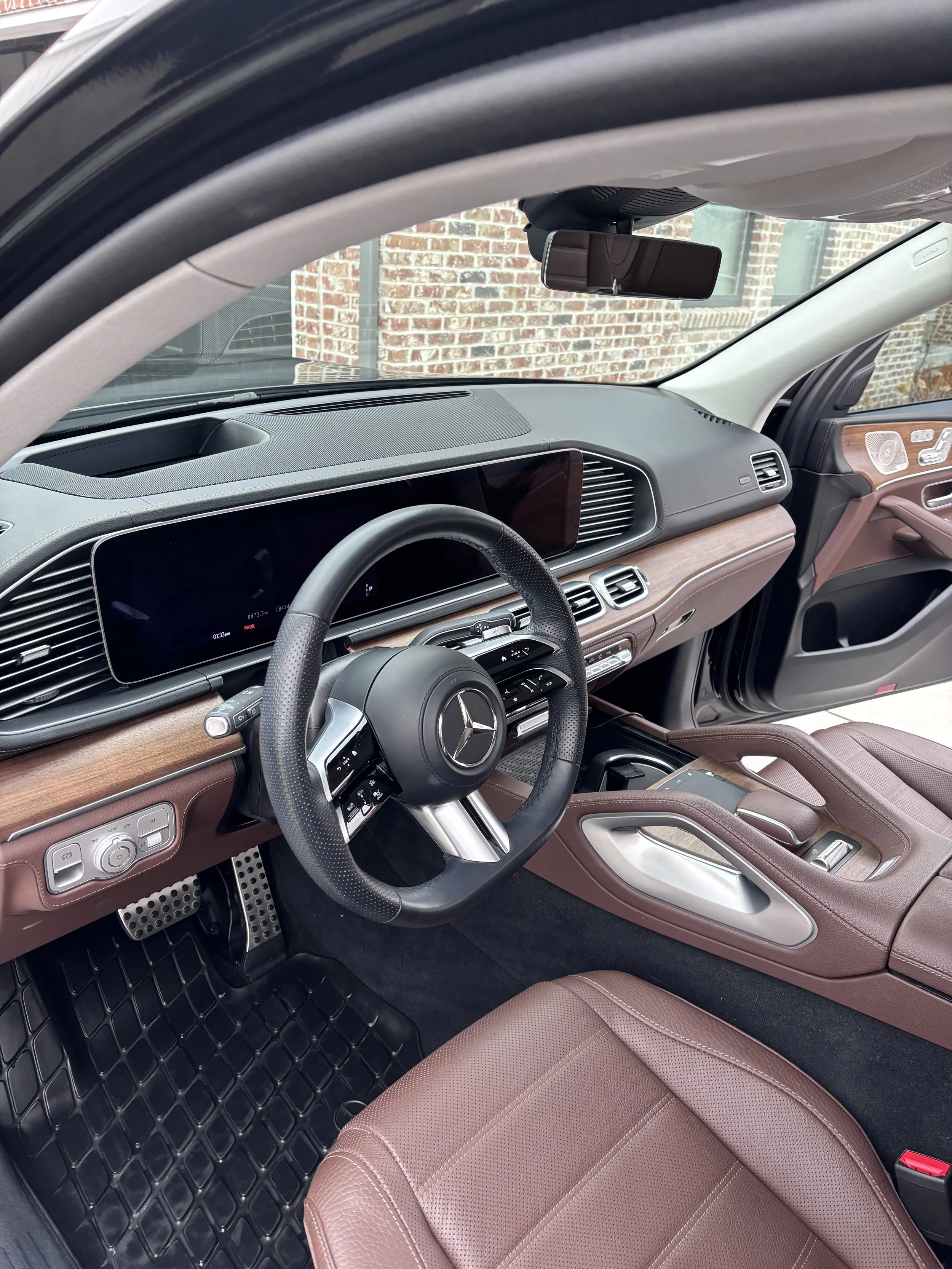 Interior of a luxury Mercedes-Benz vehicle with a black steering wheel, digital dashboard, and tan leather seats.