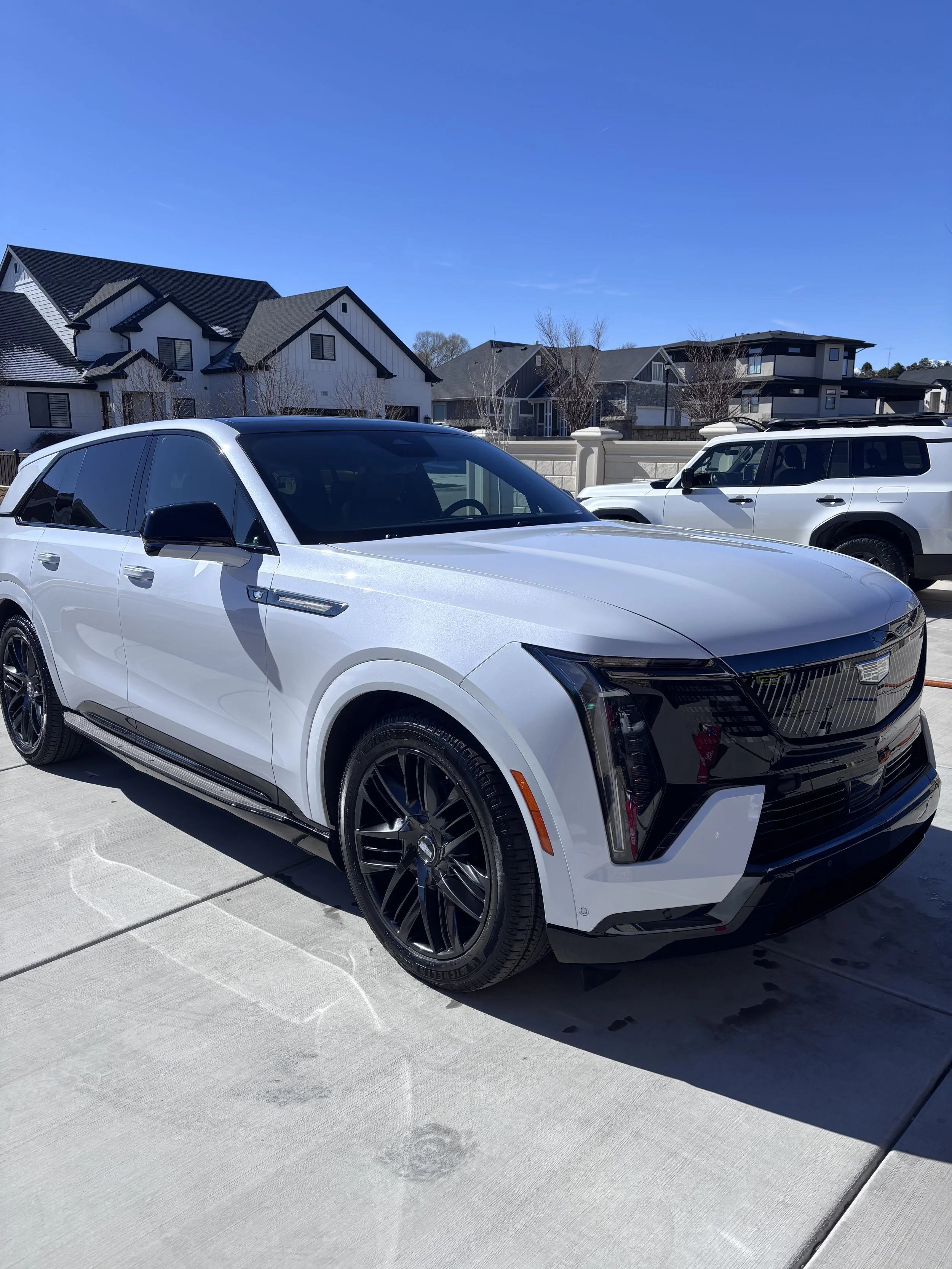 A white electric SUV parked in a driveway with modern houses and a clear blue sky in the background.