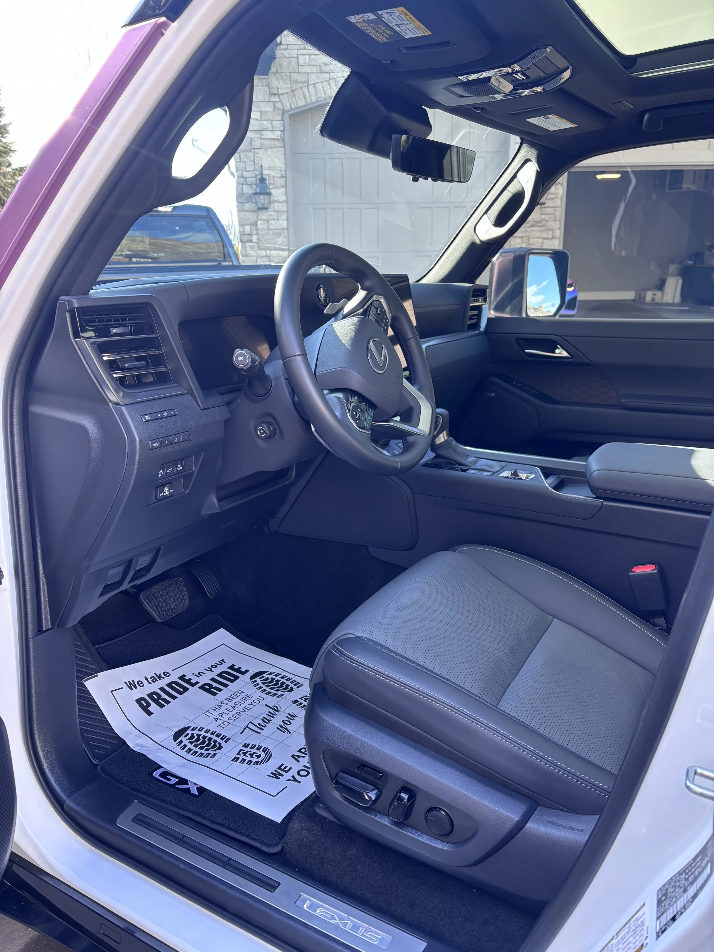 Interior of a Lexus vehicle showing the driver's seat, steering wheel, dashboard, and part of the passenger seat from the open driver's side door.