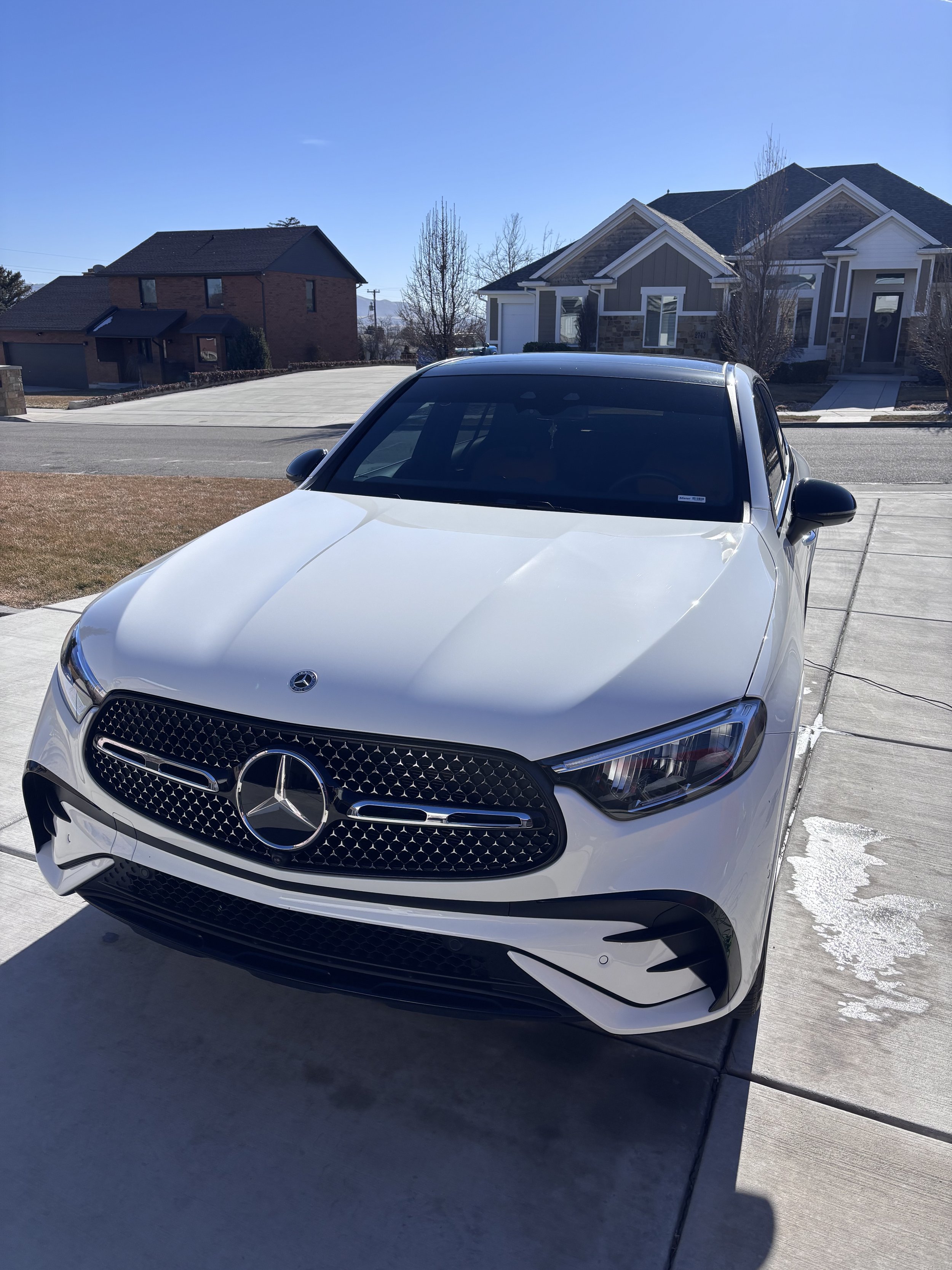A white Mercedes-Benz sedan parked on a driveway in front of a suburban house on a clear sunny day.