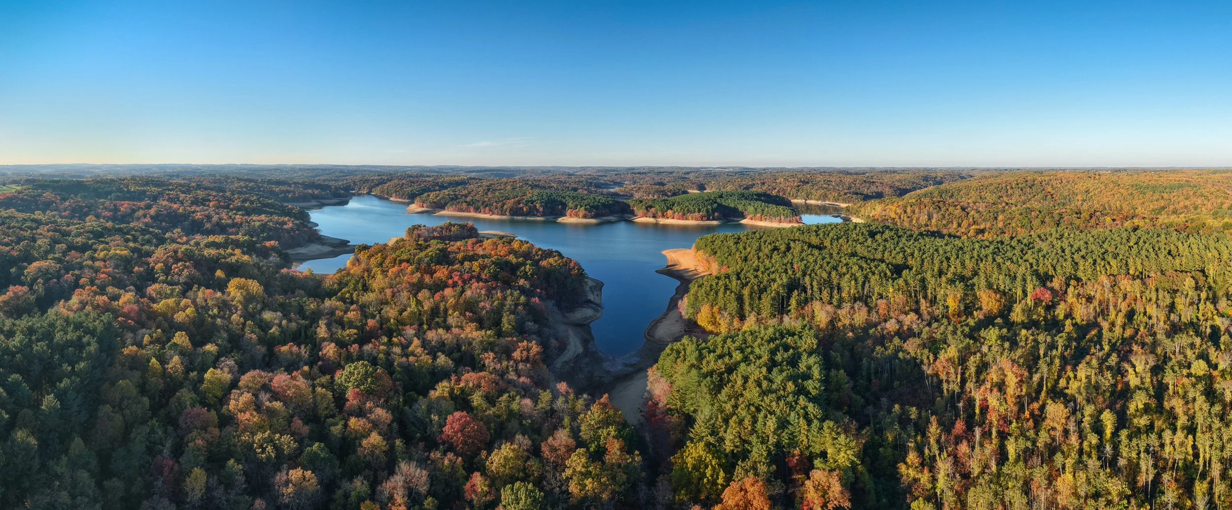 Aerial panorama of the northern section of Prettyboy Reservoir in Baltimore County, Maryland, surrounded by peak fall foliage, with low water exposing the shorelines.