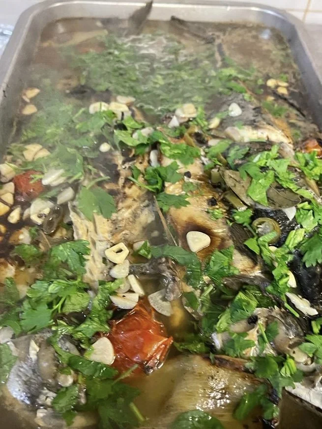 A tray of cooked fish topped with chopped garlic, fresh herbs, and garnished with a whole cooked crab.