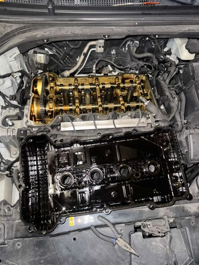 Open car engine with valve cover removed, showing camshaft and valve train components